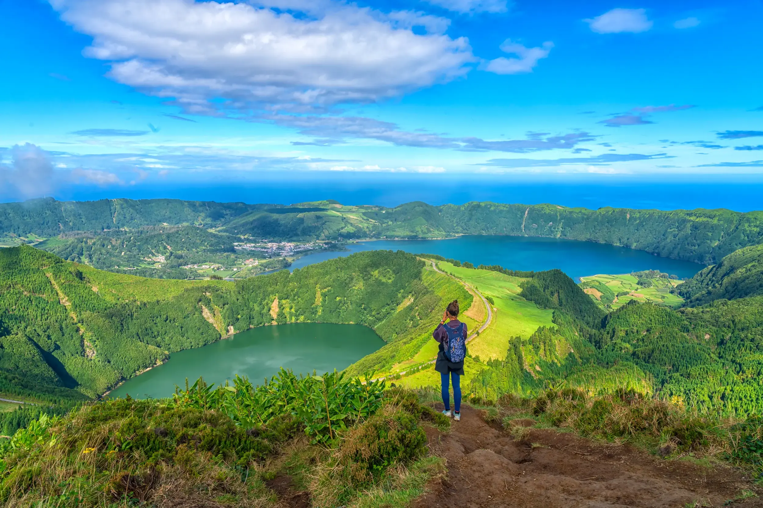 Eine Wanderin am Vista do Rei genießt den Ausblick auf die Vulkanseen Lagoa Azul und Lagoa Verde in der Caldeira von Sete Cidades.