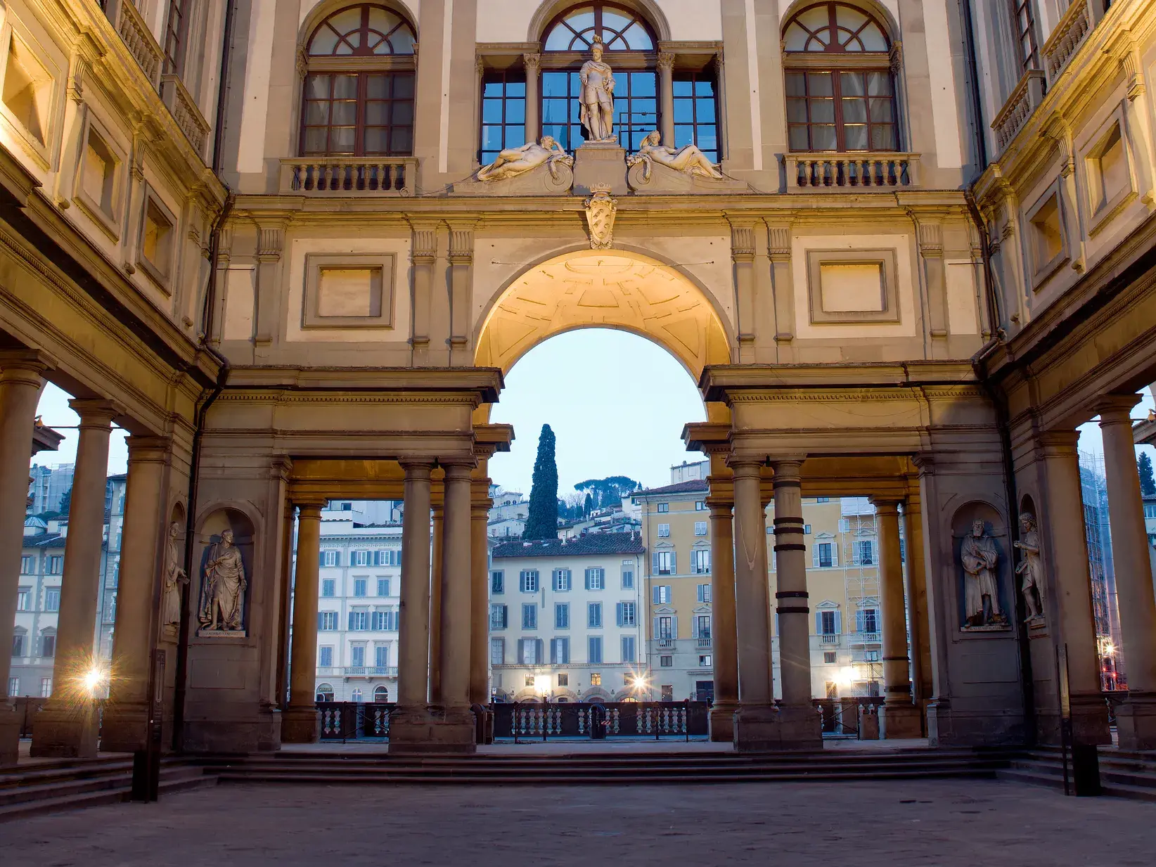 Der Säulenhof der Uffizien in Florenz mit Blick durch einen Rundbogen auf historische Fassaden bei Dämmerung.
