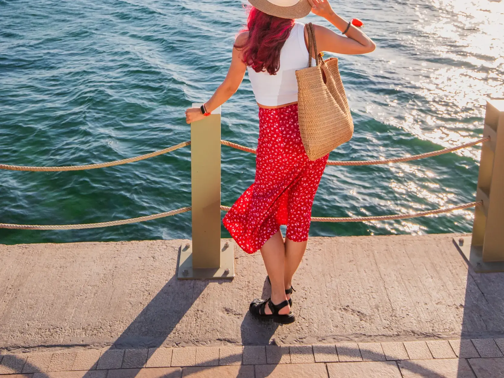 Eine Frau im Sommer-Outfit genießt auf einer Uferpromenade in Istanbul den sonnigen Ausblick über den glitzernden Bosporus.