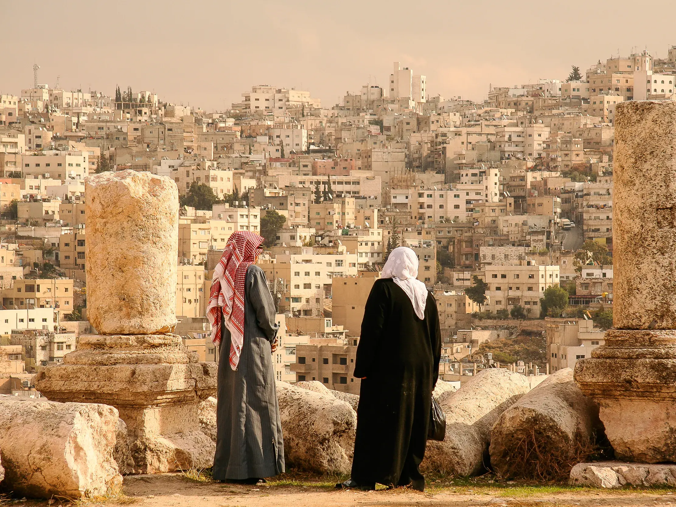 Panoramablick von der Zitadelle Amman: Zwei Personen in traditioneller Kleidung betrachten die dicht bebauten Hügel der Hauptstadt.