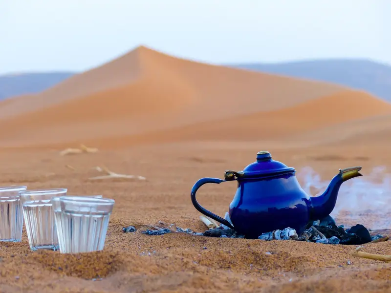 Traditionelle Teezeremonie mit einer blauen Kanne auf Glut in den Sanddünen des Erg Admer in der algerischen Sahara.