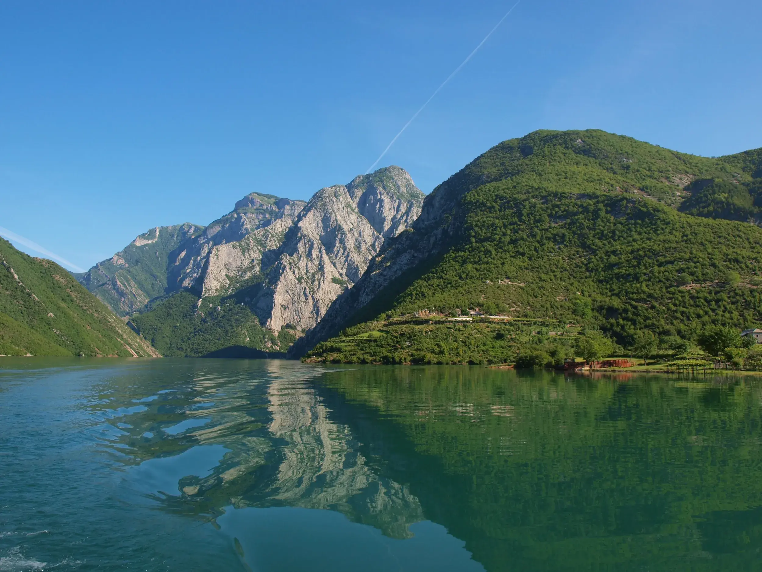Grüne und schroffe Berge der albanischen Alpen spiegeln sich bei einer Fährfahrt auf dem türkisen Koman-Stausee.