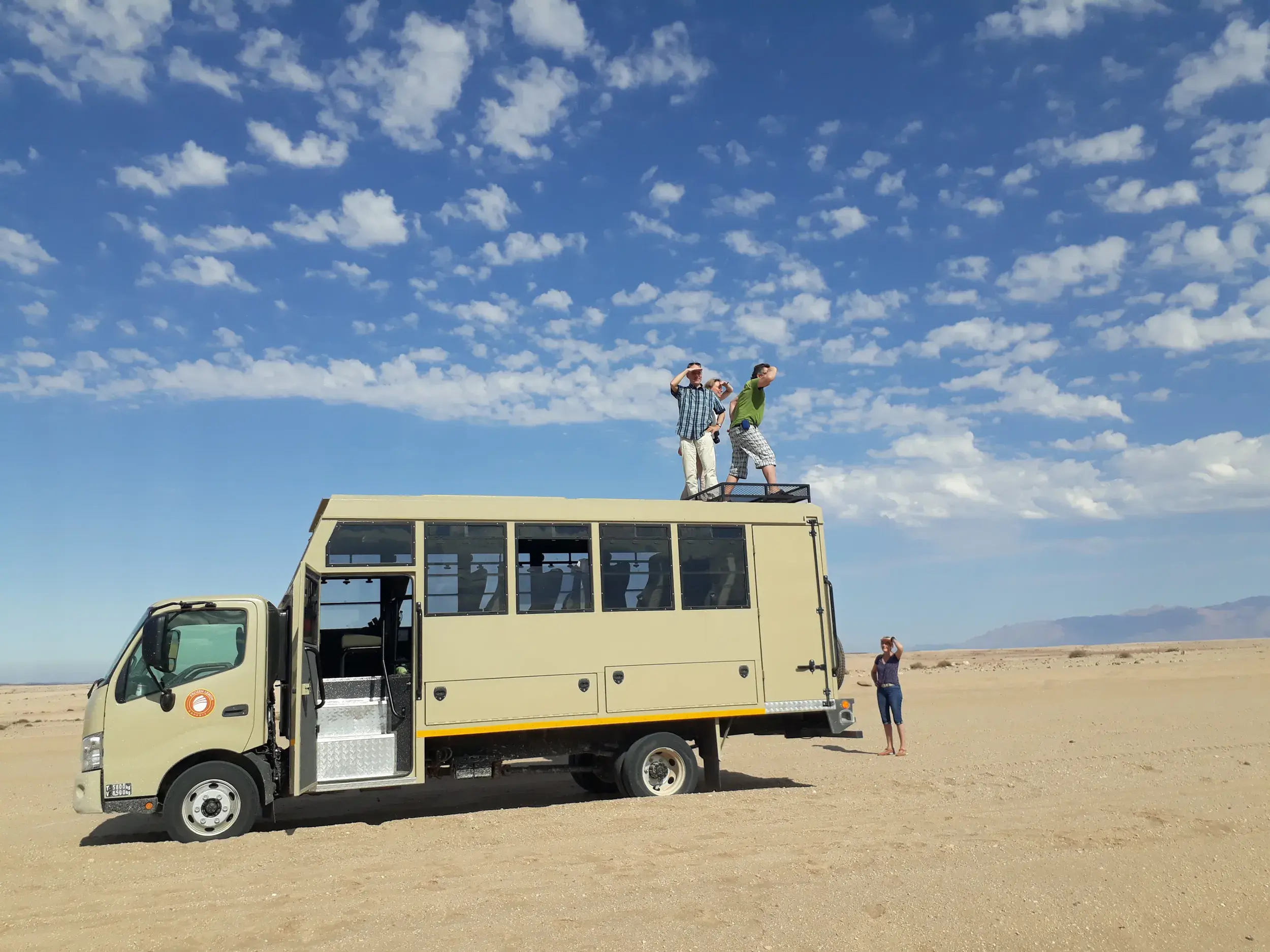 Reisende blicken vom Dach ihres Safari-Trucks in die endlose Weite der Namib-Wüste während einer Trekkingreise in Namibia.