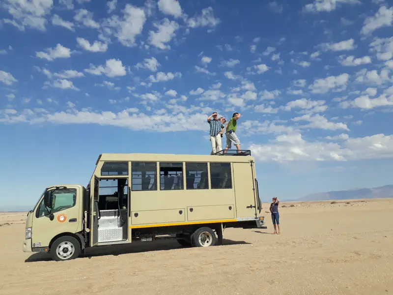 Zwei Männer einer Trekkingreise stehen auf dem Dach eines Safari-Trucks und blicken über die weite Wüstenlandschaft Namibias.