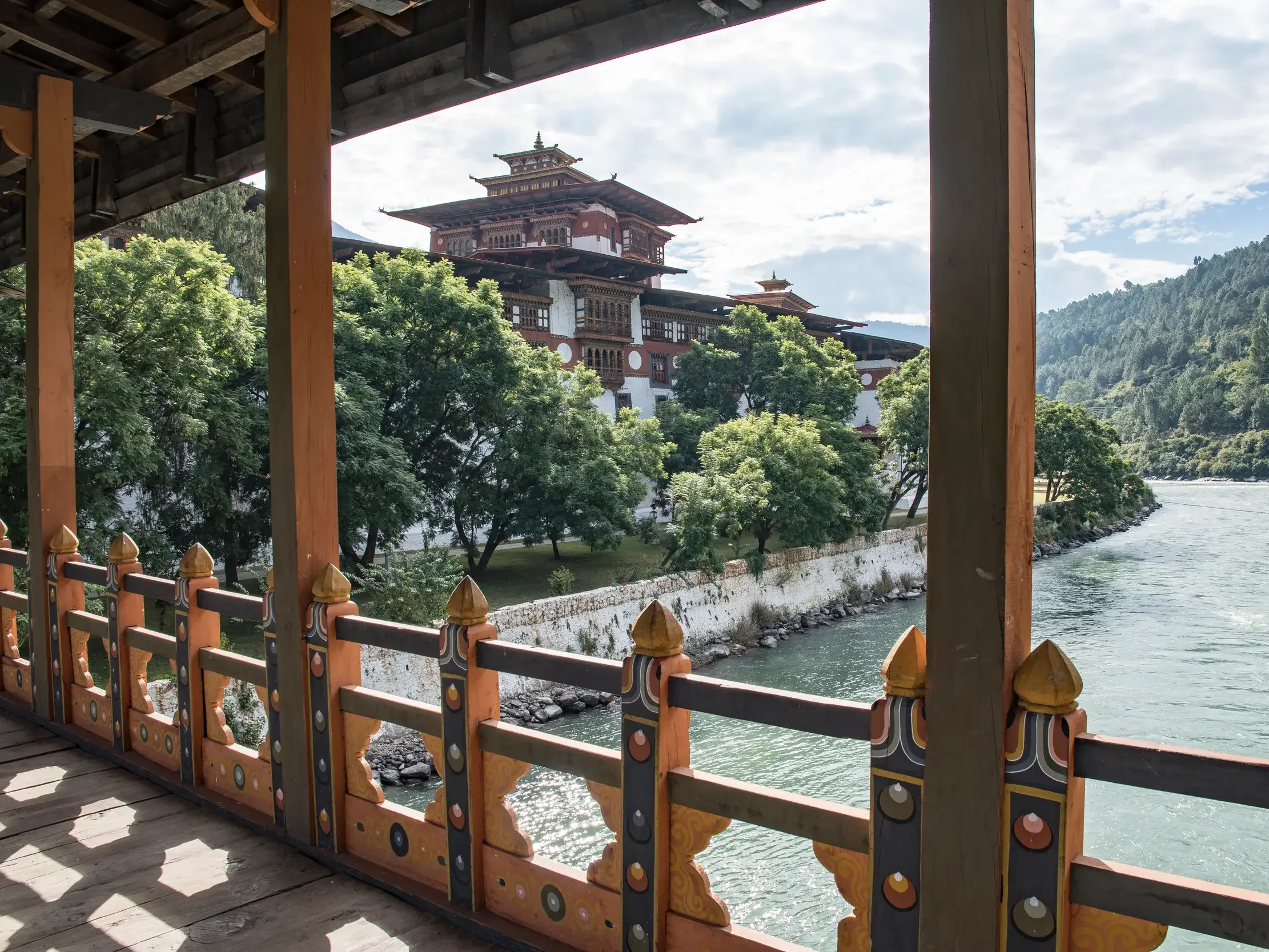 Blick von einer traditionellen Holzbrücke auf die malerische Klosterburg Punakha Dzong am Ufer des Mo Chu Flusses in Bhutan.