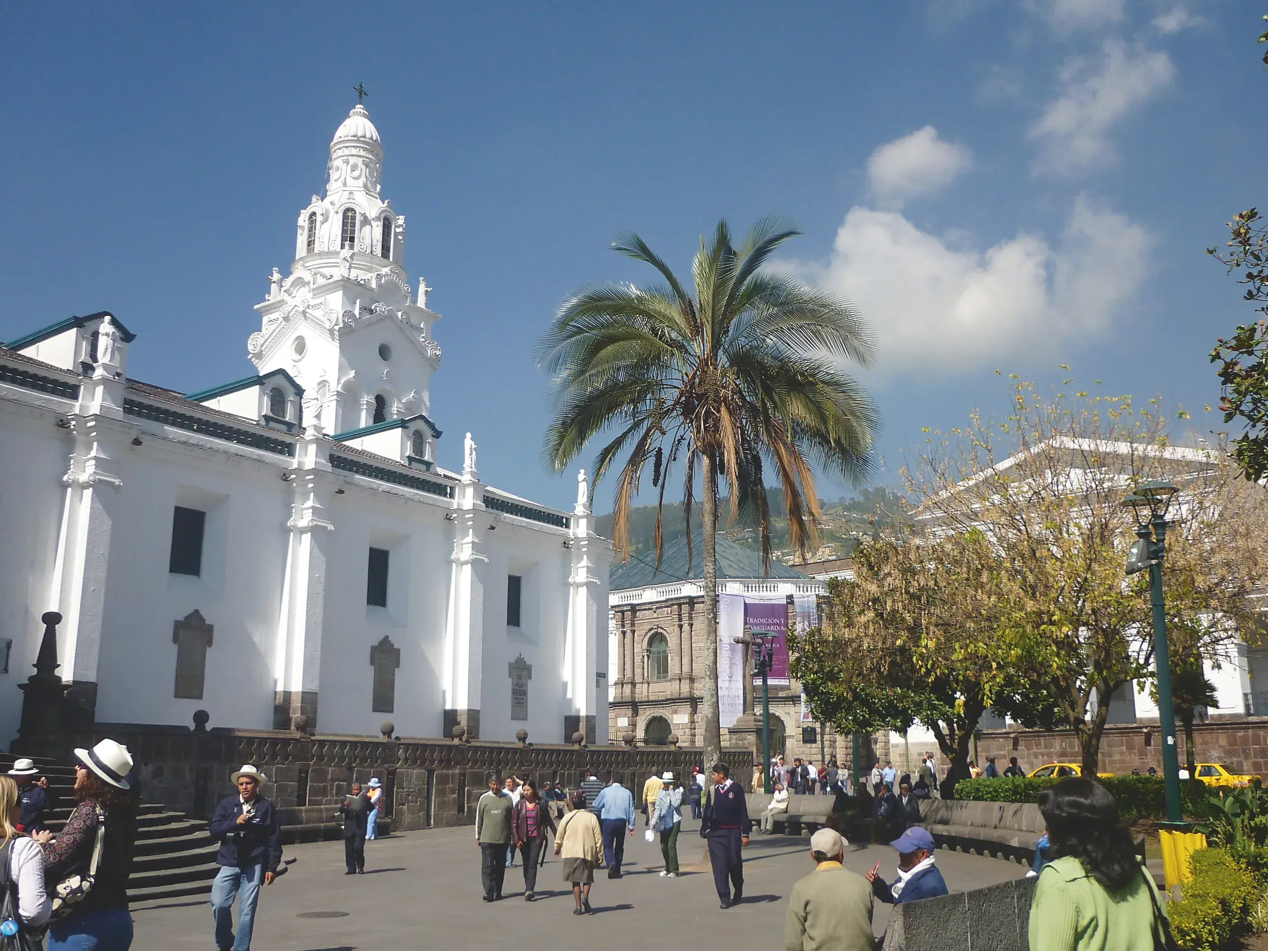 Reisende spazieren an einem sonnigen Tag an einer prachtvollen weißen Kolonialkirche vorbei in der historischen Altstadt von Quito.