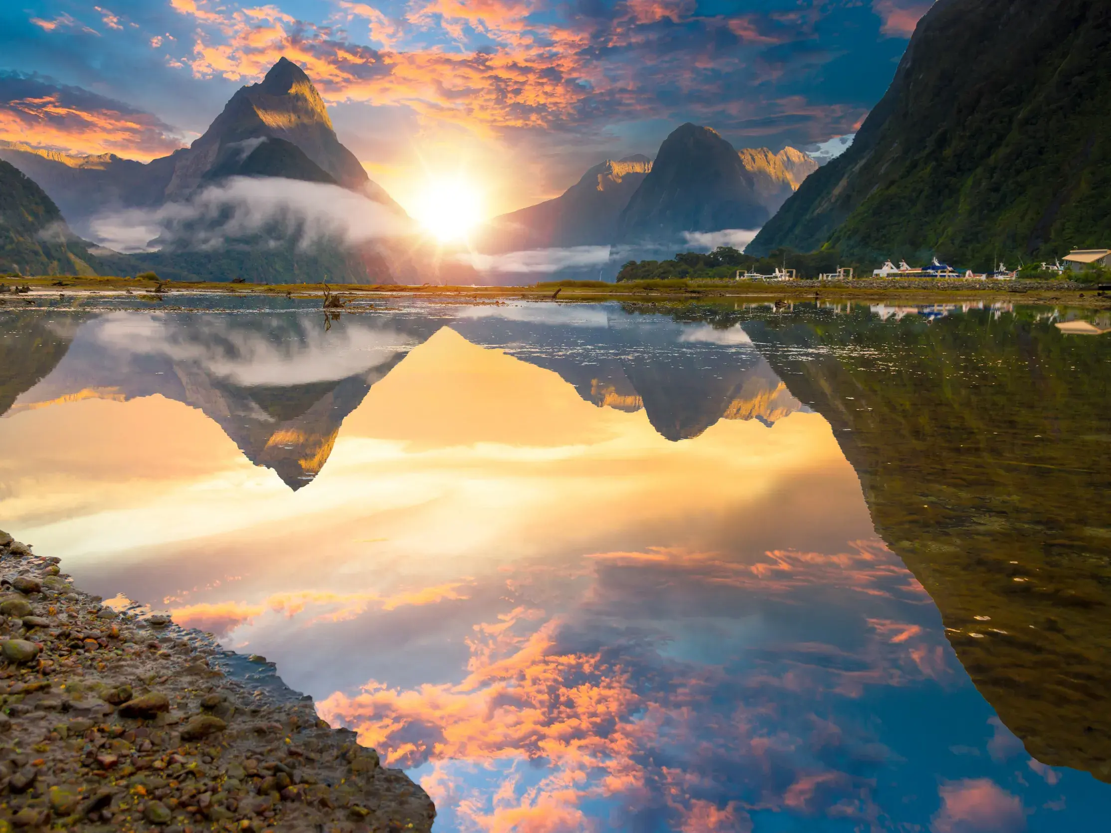 Goldener Sonnenaufgang über dem Mitre Peak im Fjordland-Nationalpark, der sich perfekt im Milford Sound spiegelt.