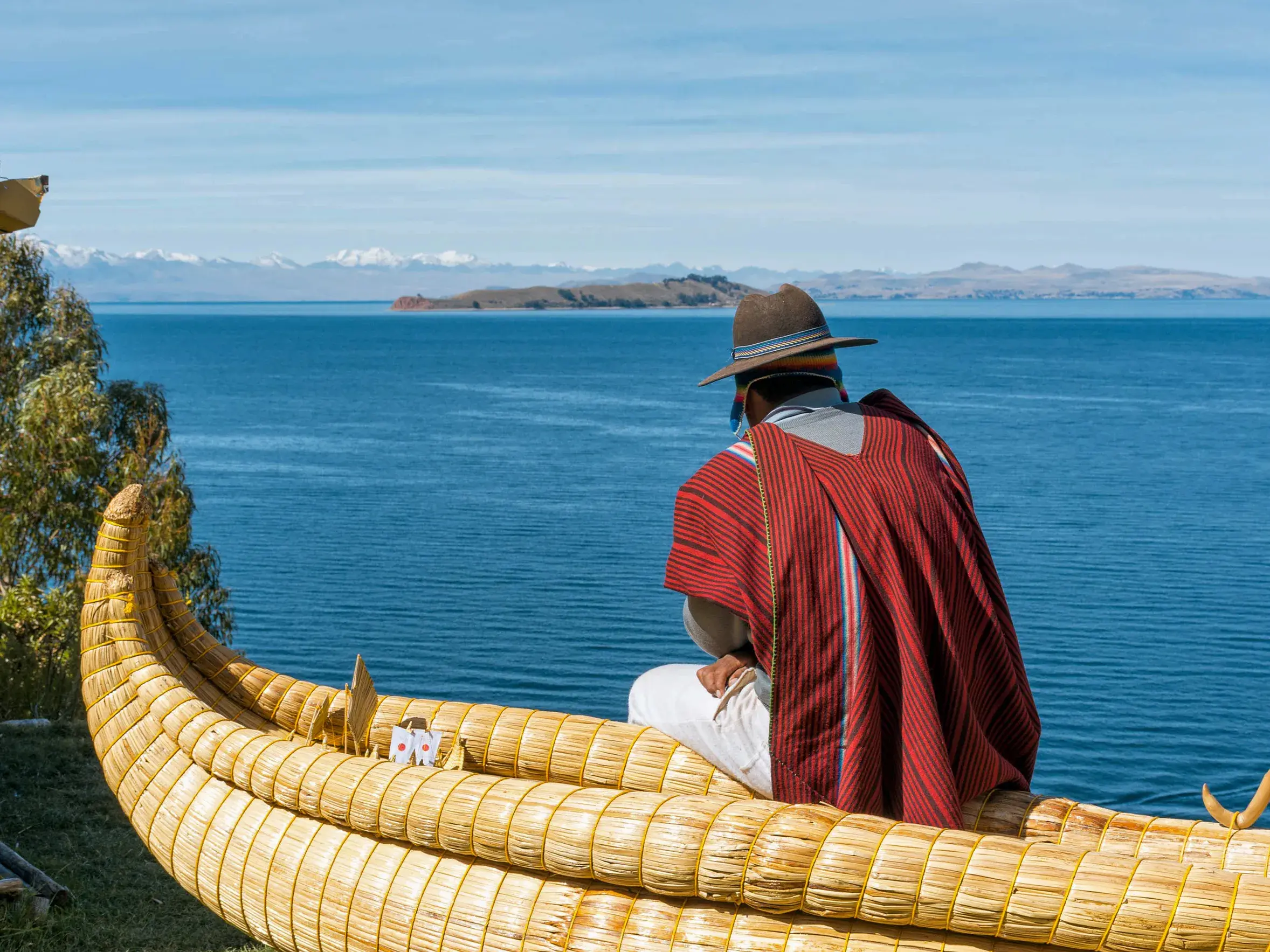 Ein Mitglied des Uru-Volkes in einem traditionellen Binsenboot auf dem Titicacasee mit den Anden am Horizont.