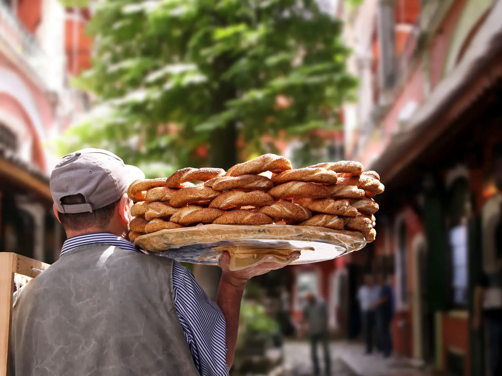 Ein Straßenverkäufer balanciert ein großes Tablett mit frischen Simit-Sesamringen auf seiner Schulter in einer Gasse in Istanbul.