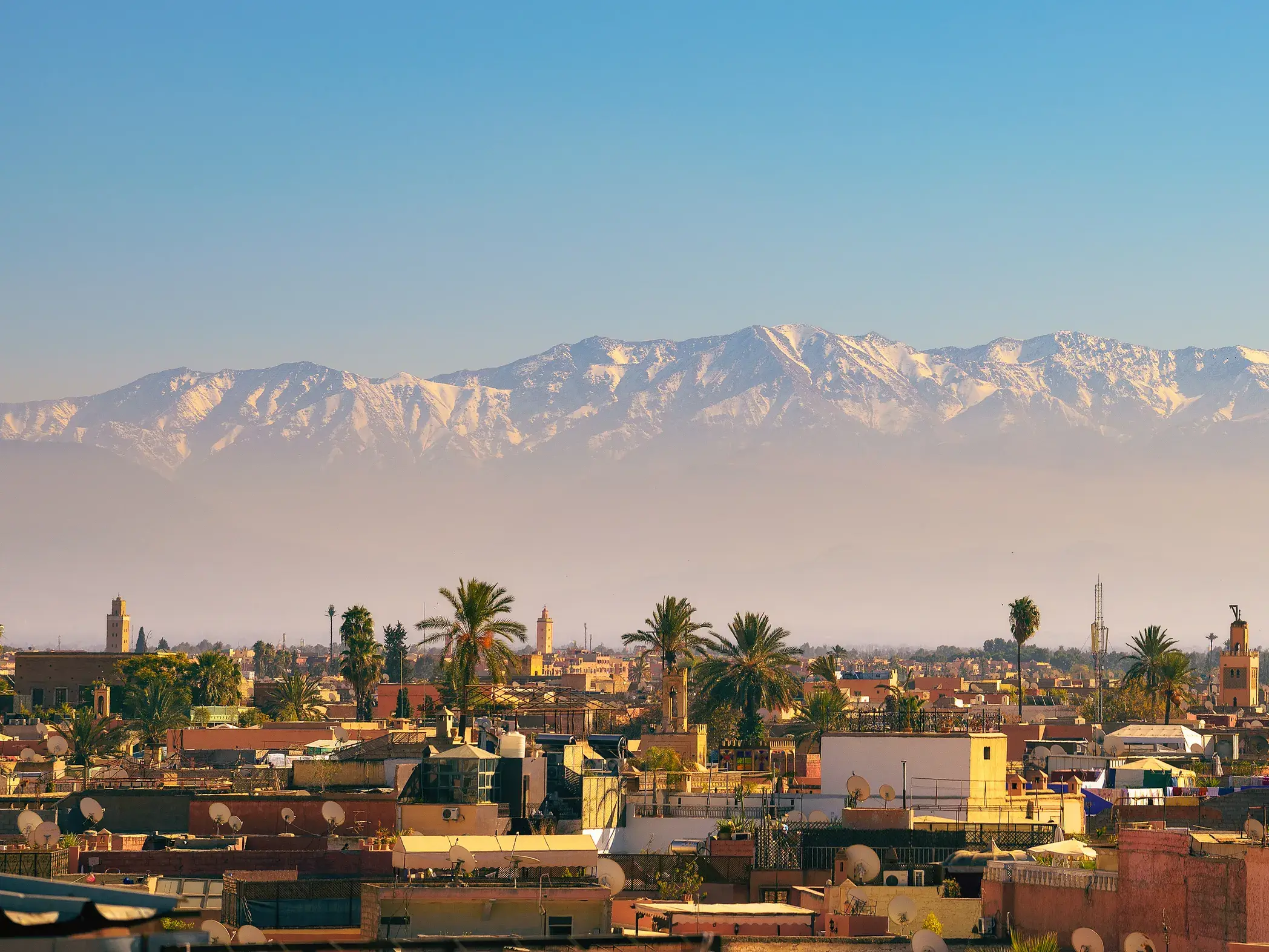 Blick über die Dächer von Marrakesch auf die schneebedeckten Gipfel des Hohen Atlas, Ziel einer Trekkingreise in Marokko.