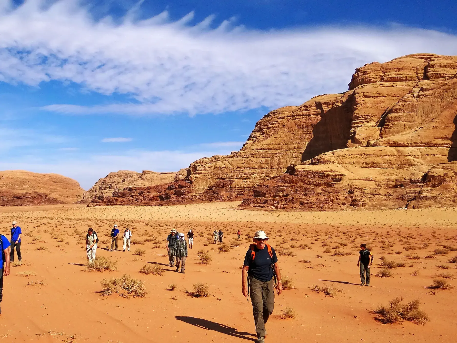Eine Hauser-Trekkinggruppe wandert durch die rote Wüstenlandschaft des Wadi Rum in Jordanien, vorbei an massiven Sandsteinbergen.