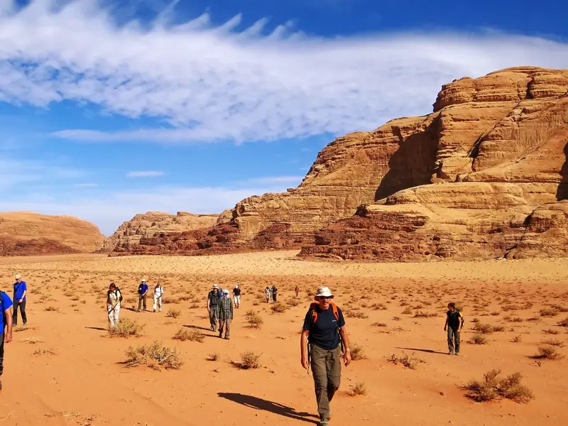 Eine Hauser-Trekkinggruppe wandert durch die rote Wüstenlandschaft des Wadi Rum in Jordanien, vorbei an massiven Sandsteinbergen.