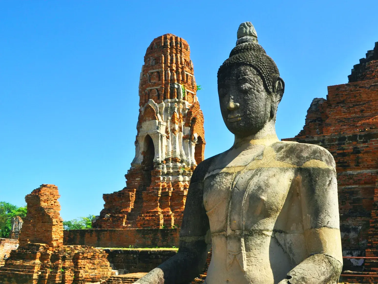 Eine verwitterte Buddha-Statue aus Stein vor den antiken Ziegelstein-Ruinen der Königsstadt Ayutthaya in Thailand.