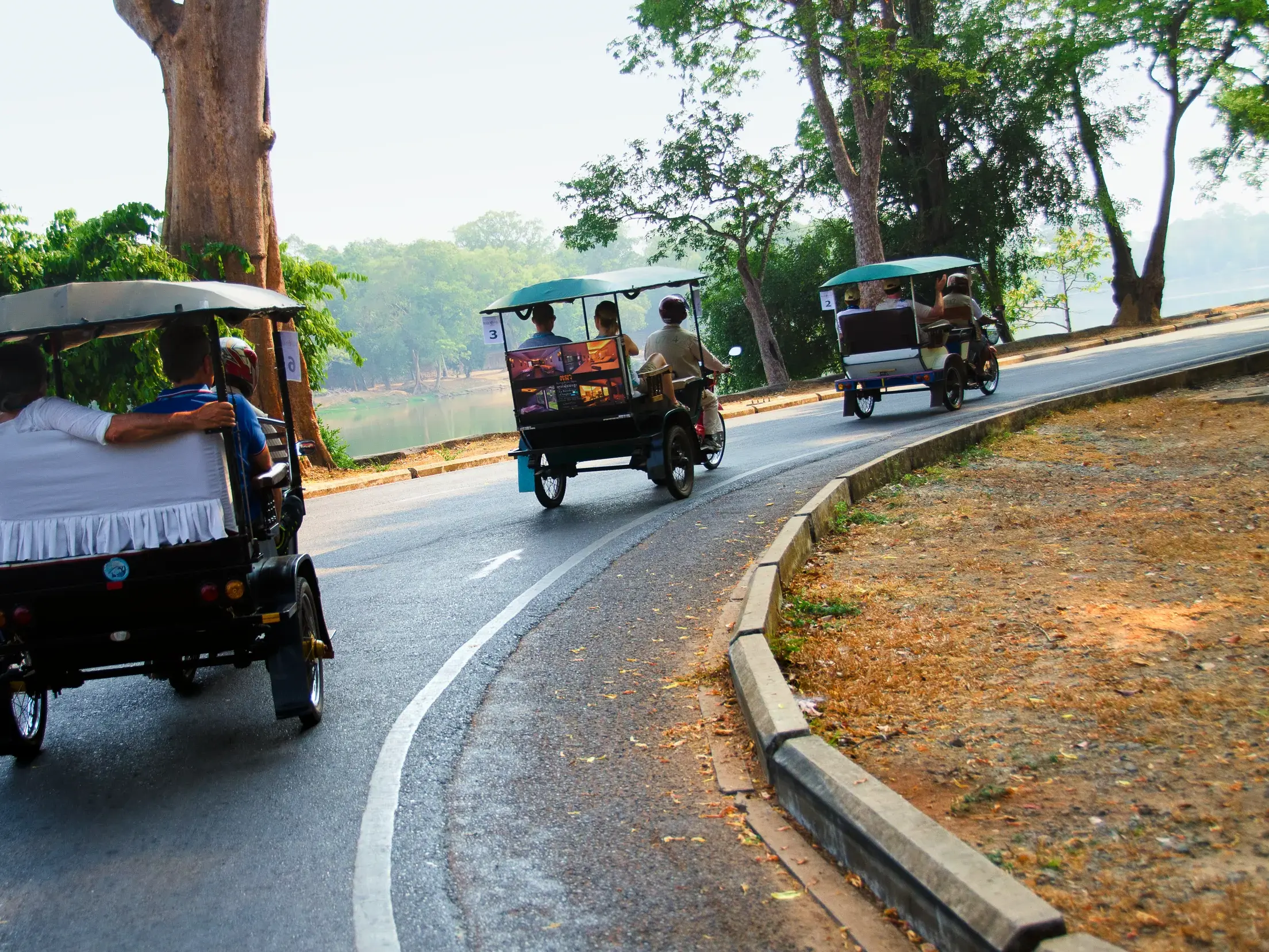 Eine geführte Gruppenreise per Tuk-Tuk auf einer kurvigen Straße durch die tropische Landschaft von Angkor in Kambodscha.