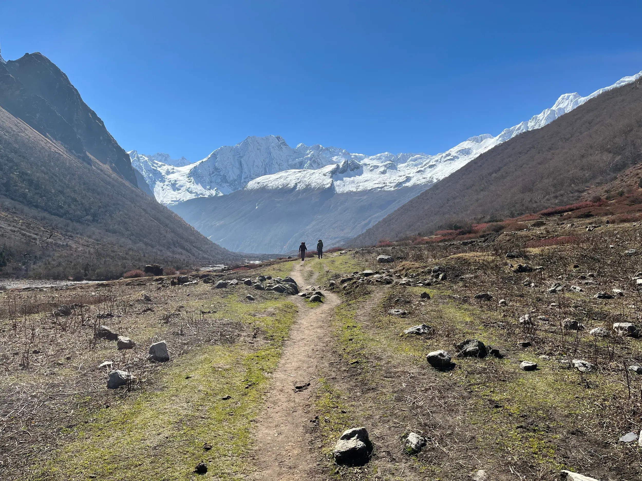 Zwei Trekker wandern auf einem Pfad durch das Buri Gandaki-Tal mit Panorama auf die schneebedeckten Gipfel des Manaslu.