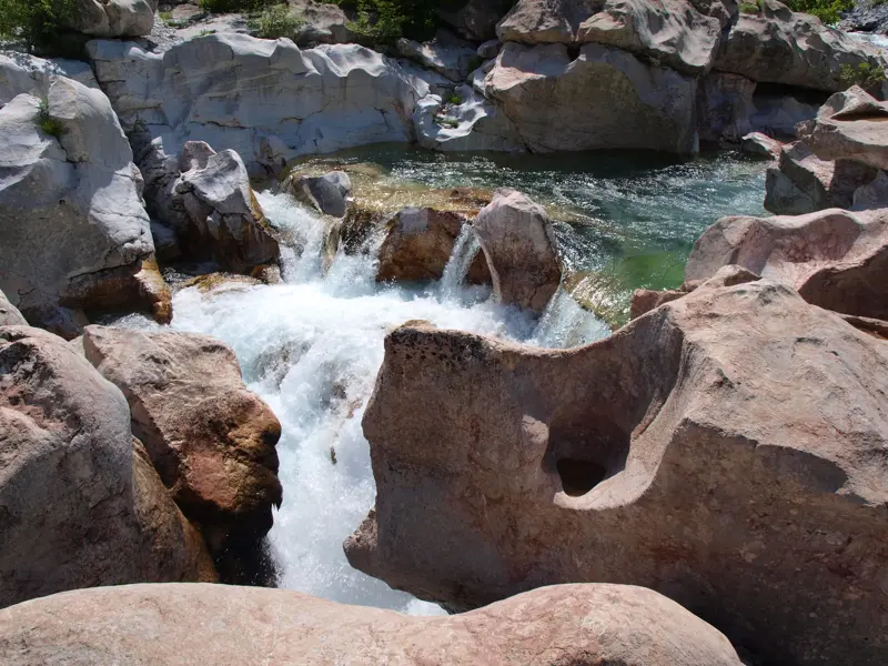 Glasklares, türkises Wasser des Blauen Auges in Albanien fließt über ausgewaschene Karstfelsen und bildet kleine Wasserfälle.