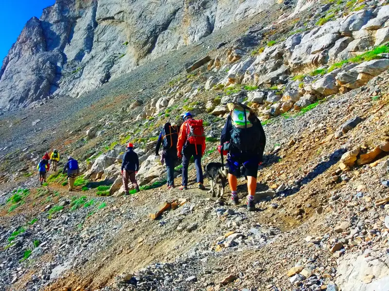 Eine Reisegruppe beim Trekking auf einem steilen Geröllpfad des E4-Wanderwegs im kargen Olymp-Massiv in Griechenland.