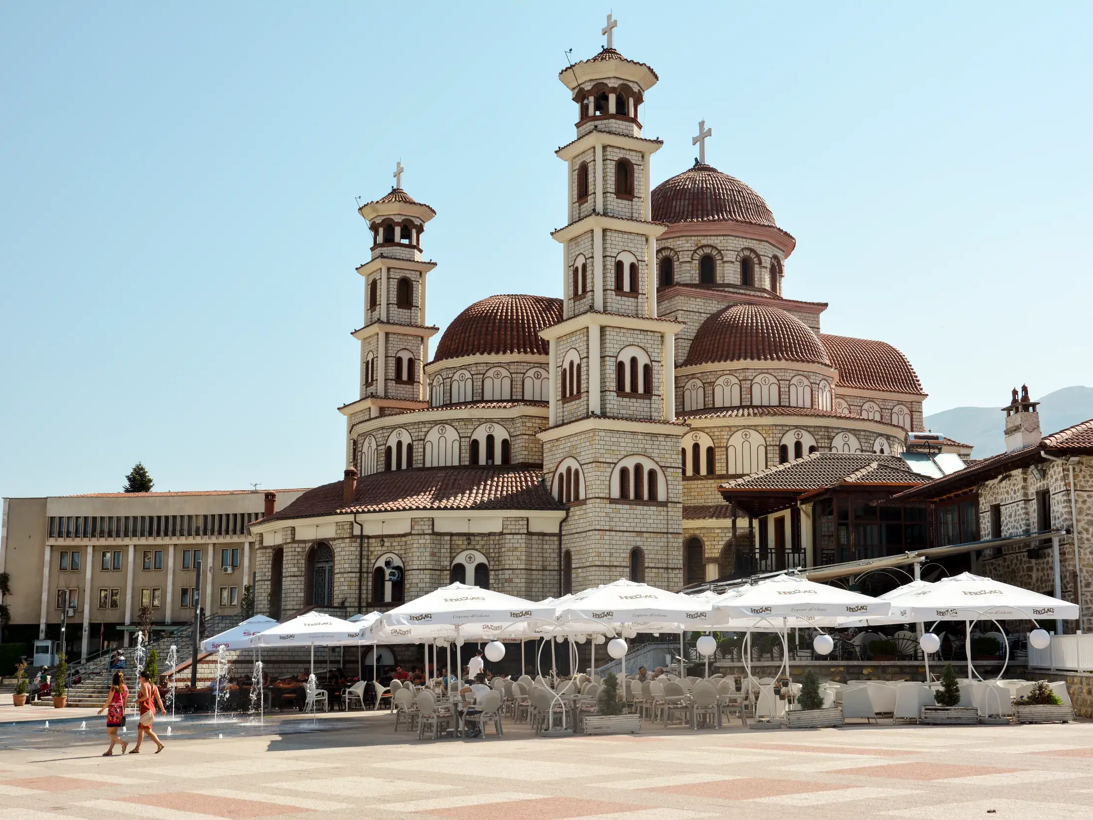 Sonnige Außenansicht der orthodoxen Auferstehungskathedrale in Korca mit einem Café im Vordergrund, ein kulturelles Highlight in Albanien.