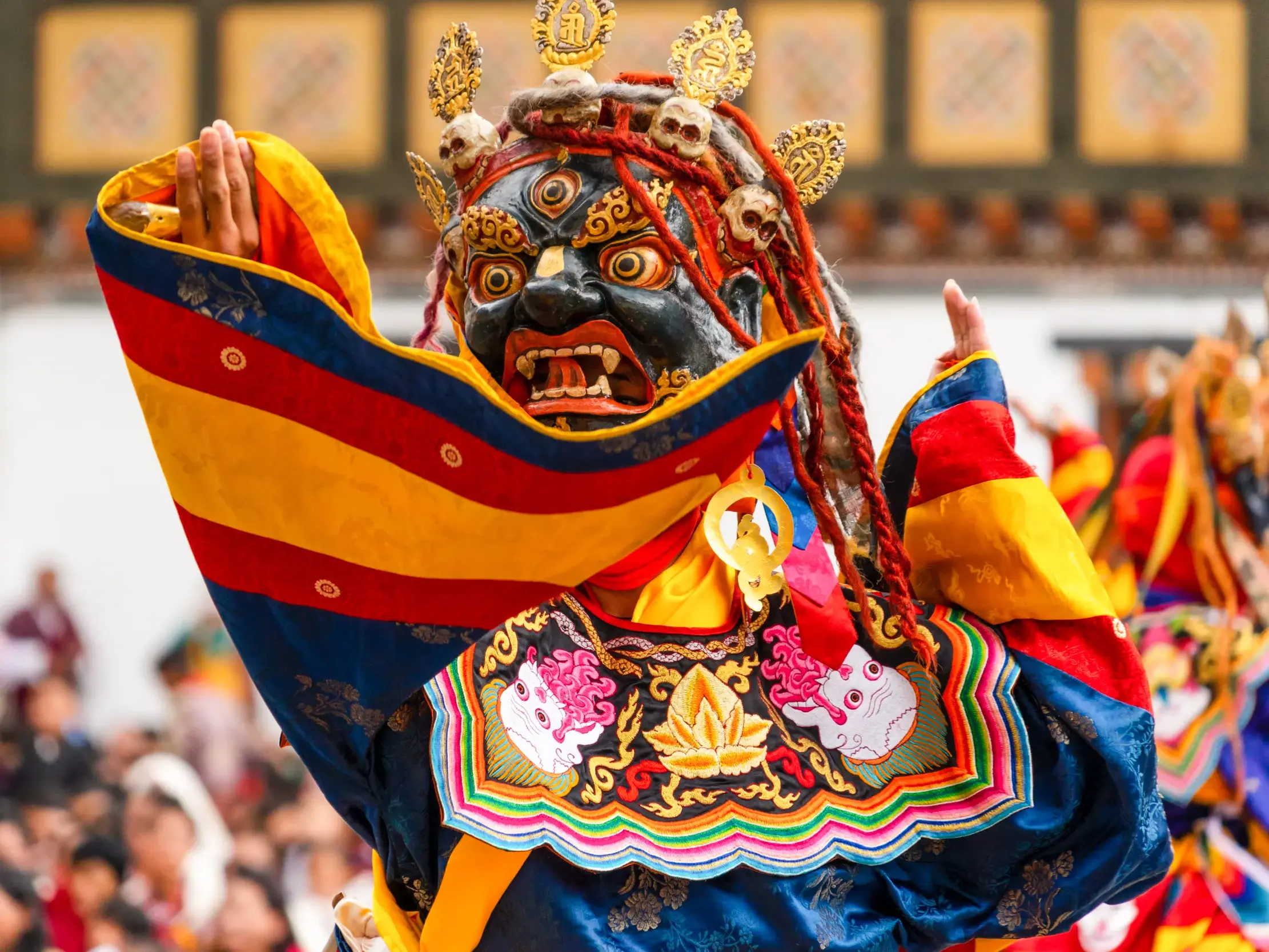 Ein Tänzer in farbenprächtigem Kostüm und Dämonenmaske führt einen rituellen Tanz beim Klosterfest in Punakha auf.