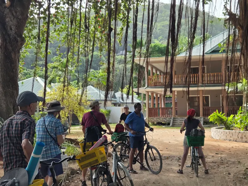 Eine Hauser-Reisegruppe mit Fahrrädern pausiert unter tropischen Bäumen für eine Besprechung mit dem Reiseleiter auf La Digue.