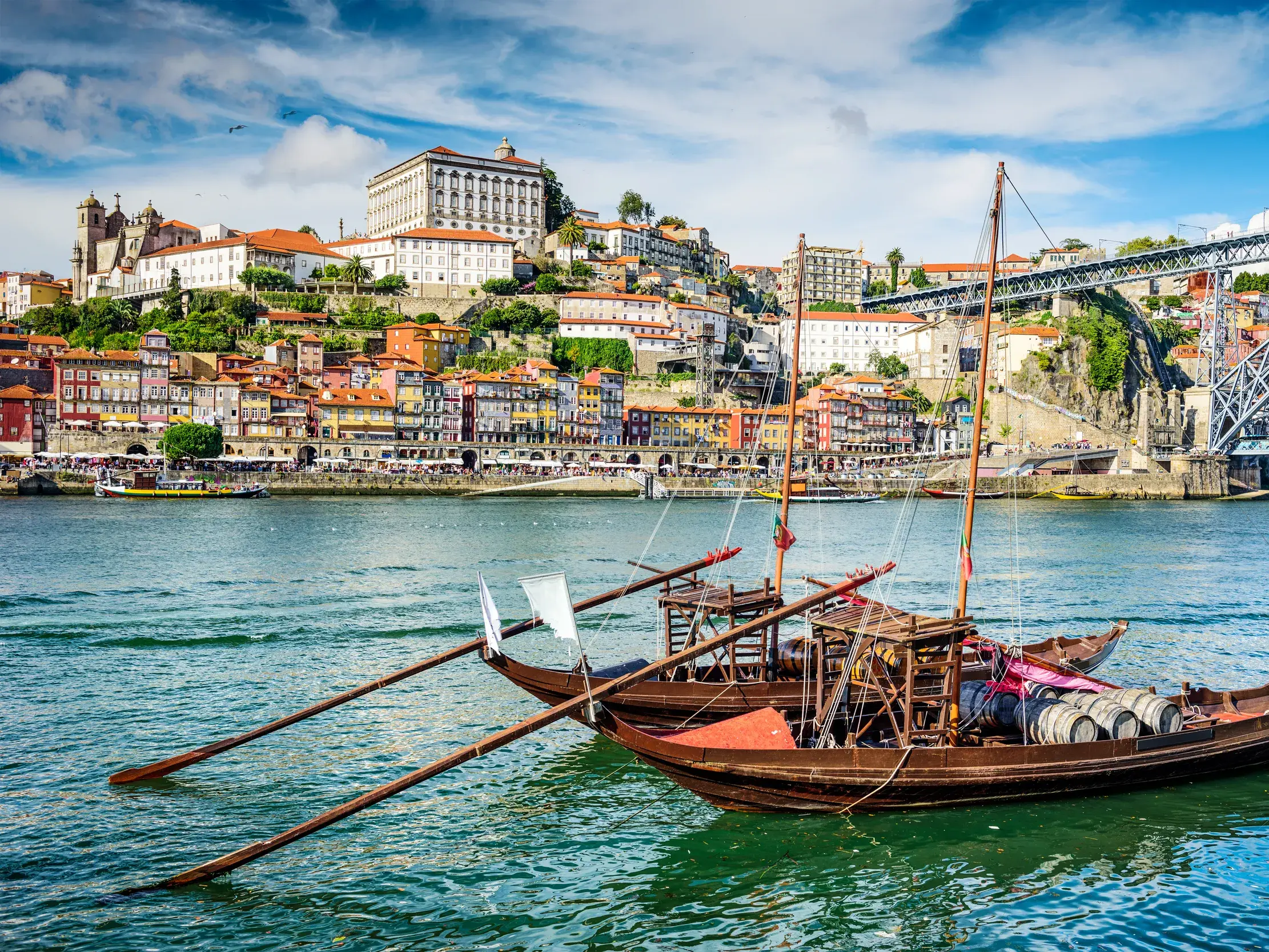 Traditionelle Portweinboote auf dem Douro vor der Kulisse des bunten Hafenviertels Ribeira in Porto bei Sonnenschein.