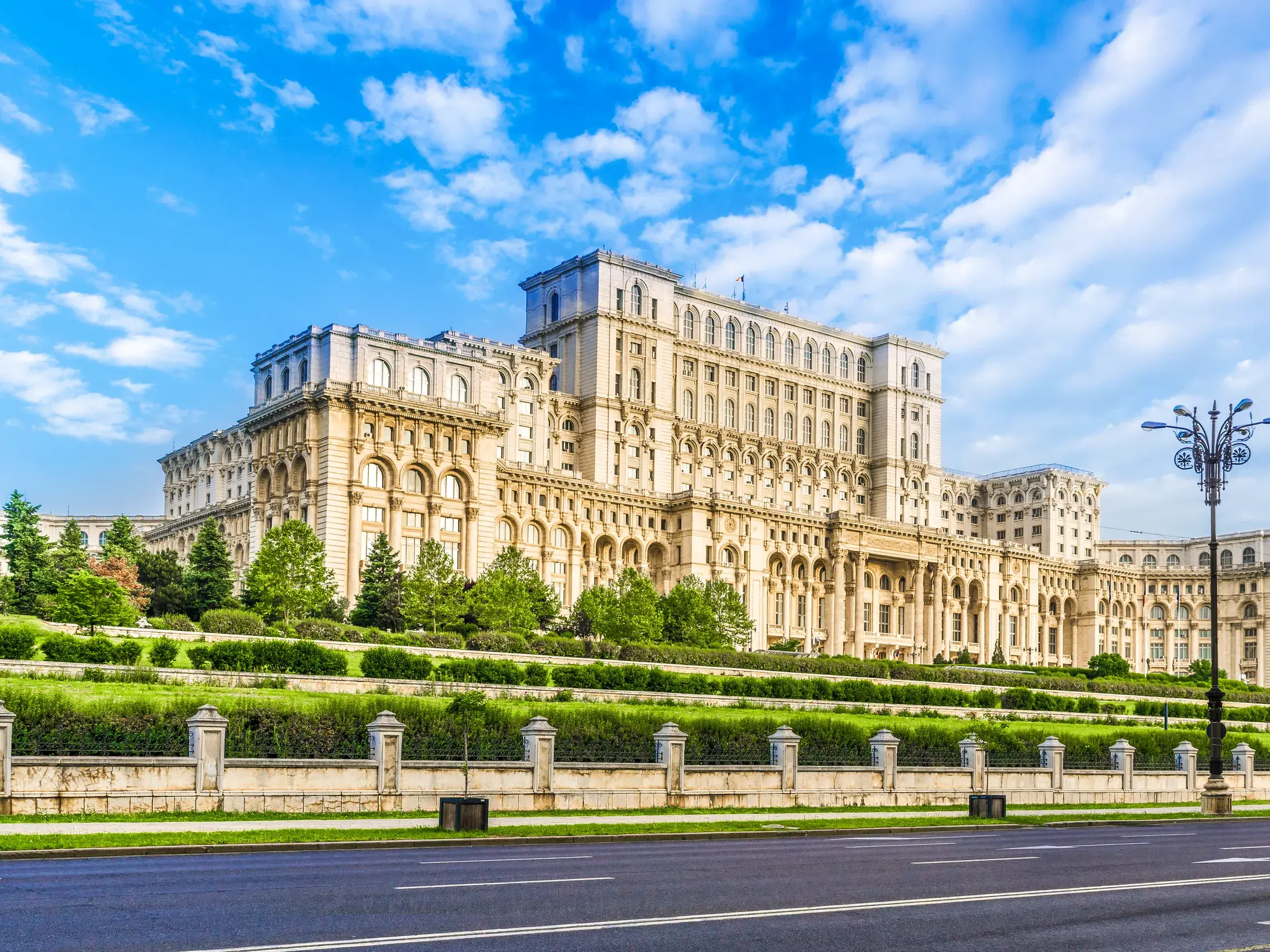 Der monumentale Parlamentspalast in Bukarest, umgeben von gepflegten Grünanlagen, unter einem strahlend blauen Himmel.