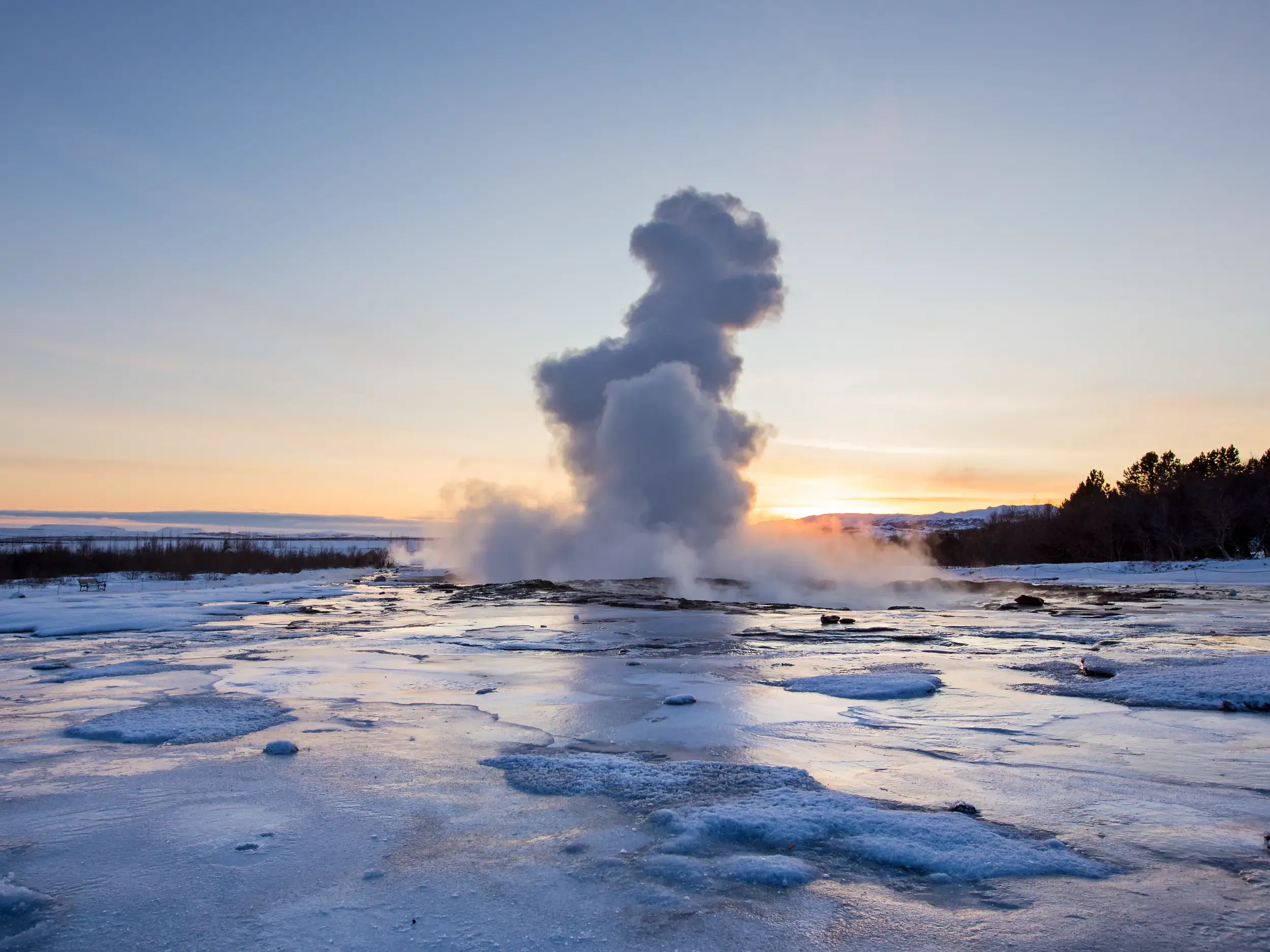 Ausbrechender Geysir Strokkur mit aufsteigender Dampfwolke in der winterlichen Landschaft Islands bei Sonnenuntergang