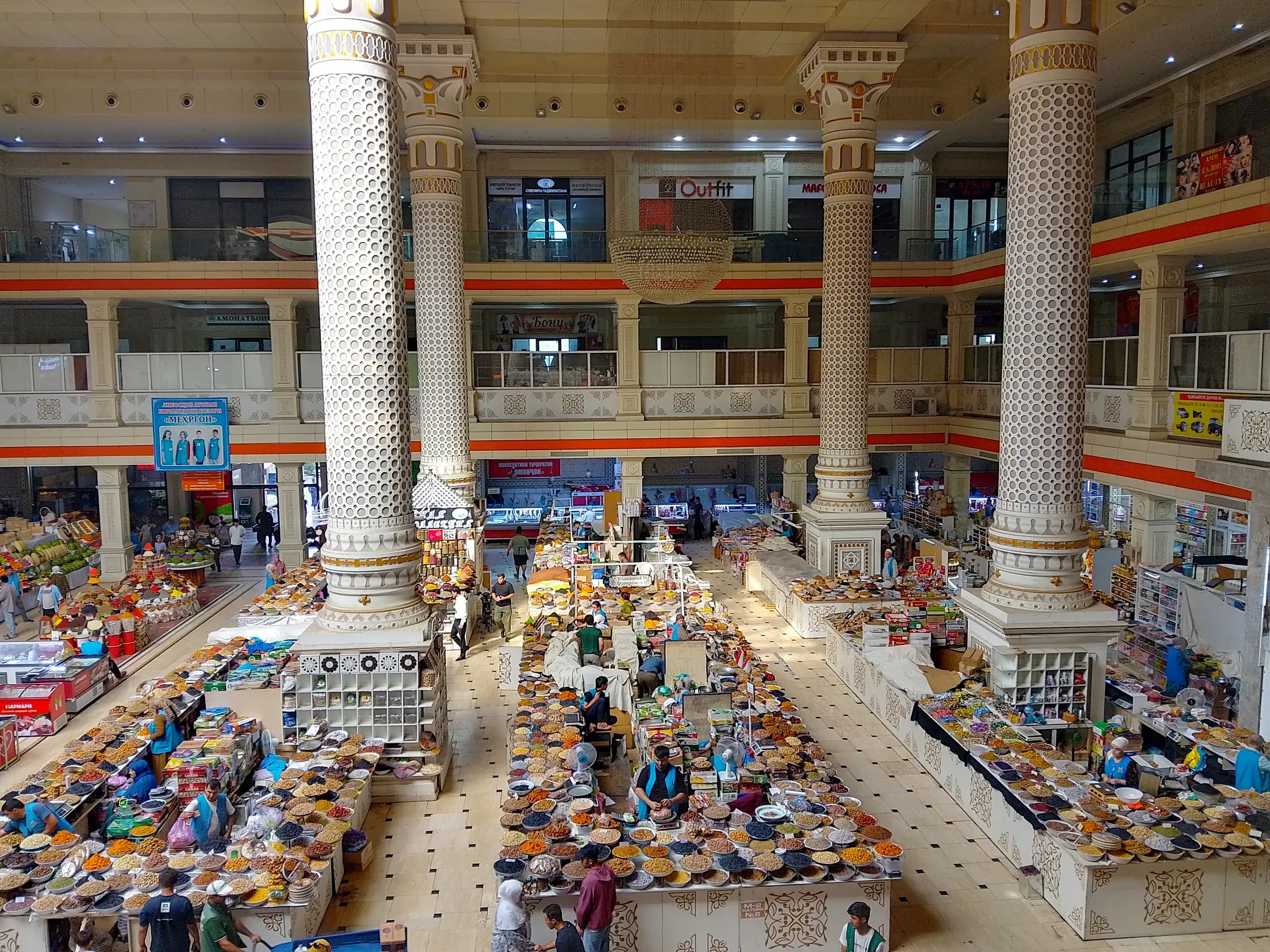 Hohe, verzierte Säulen in der belebten Markthalle des Grünen Basars in Duschanbe mit Ständen voller Trockenfrüchte und Nüsse.