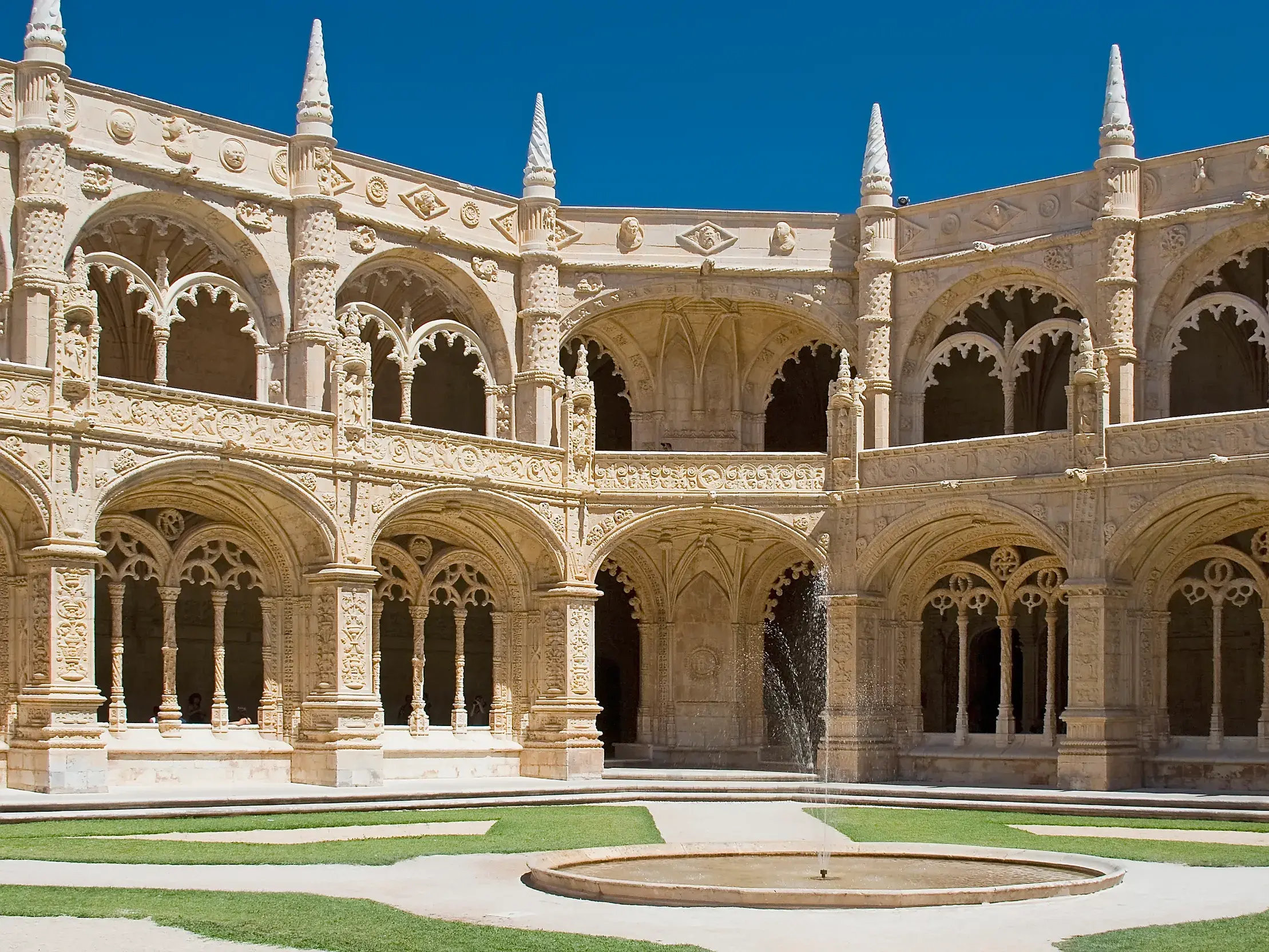 Prachtvoller Kreuzgang eines portugiesischen Klosters mit detailreichen Steinmetzarbeiten und einem Brunnen im Innenhof bei Sonne.