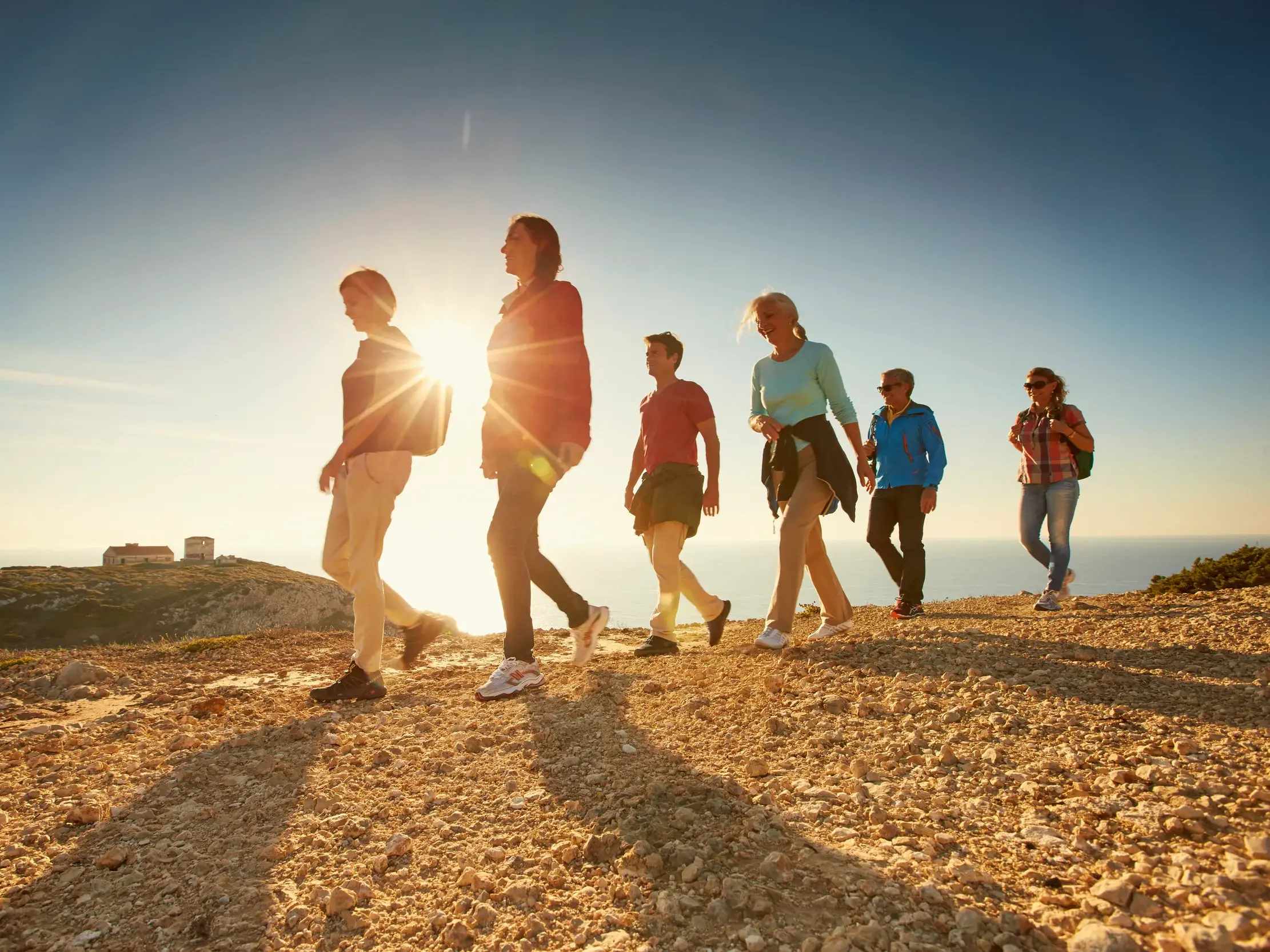 Eine Reisegruppe wandert bei Sonnenuntergang auf einem Klippenpfad an der Felsküste der Algarve mit weitem Blick über den Atlantik.