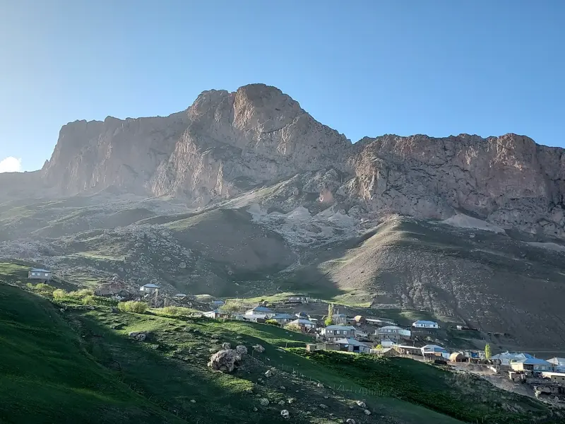 Idyllisches Bergdorf Khinaliq im Großen Kaukasus, eingebettet in sonnige, grüne Hänge unter einem imposanten Felsmassiv.