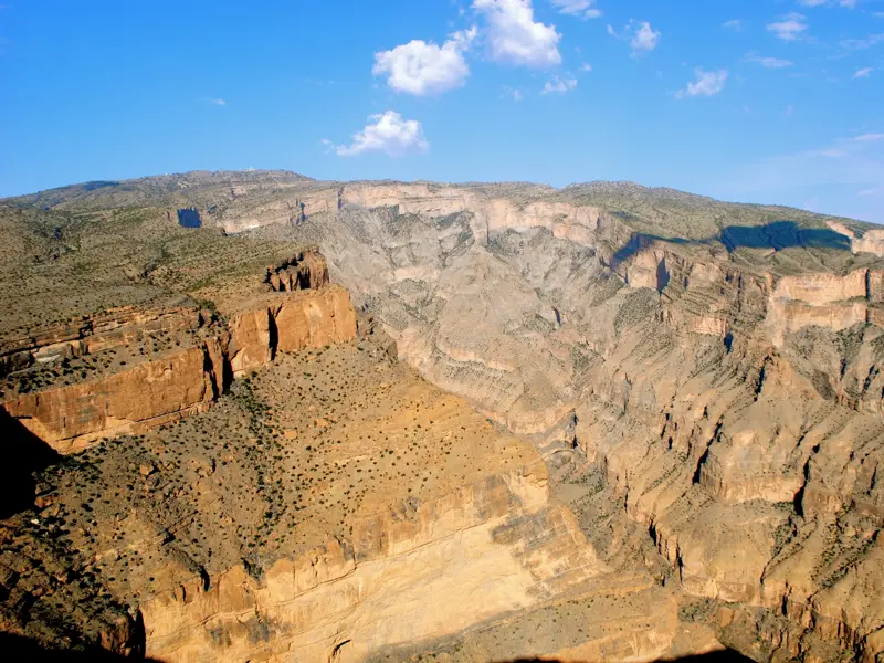 Panoramablick beim Trekking am Jebel Shams über tiefe Canyons und Hochebenen im Hadschar-Gebirge im Oman bei Sonnenschein.