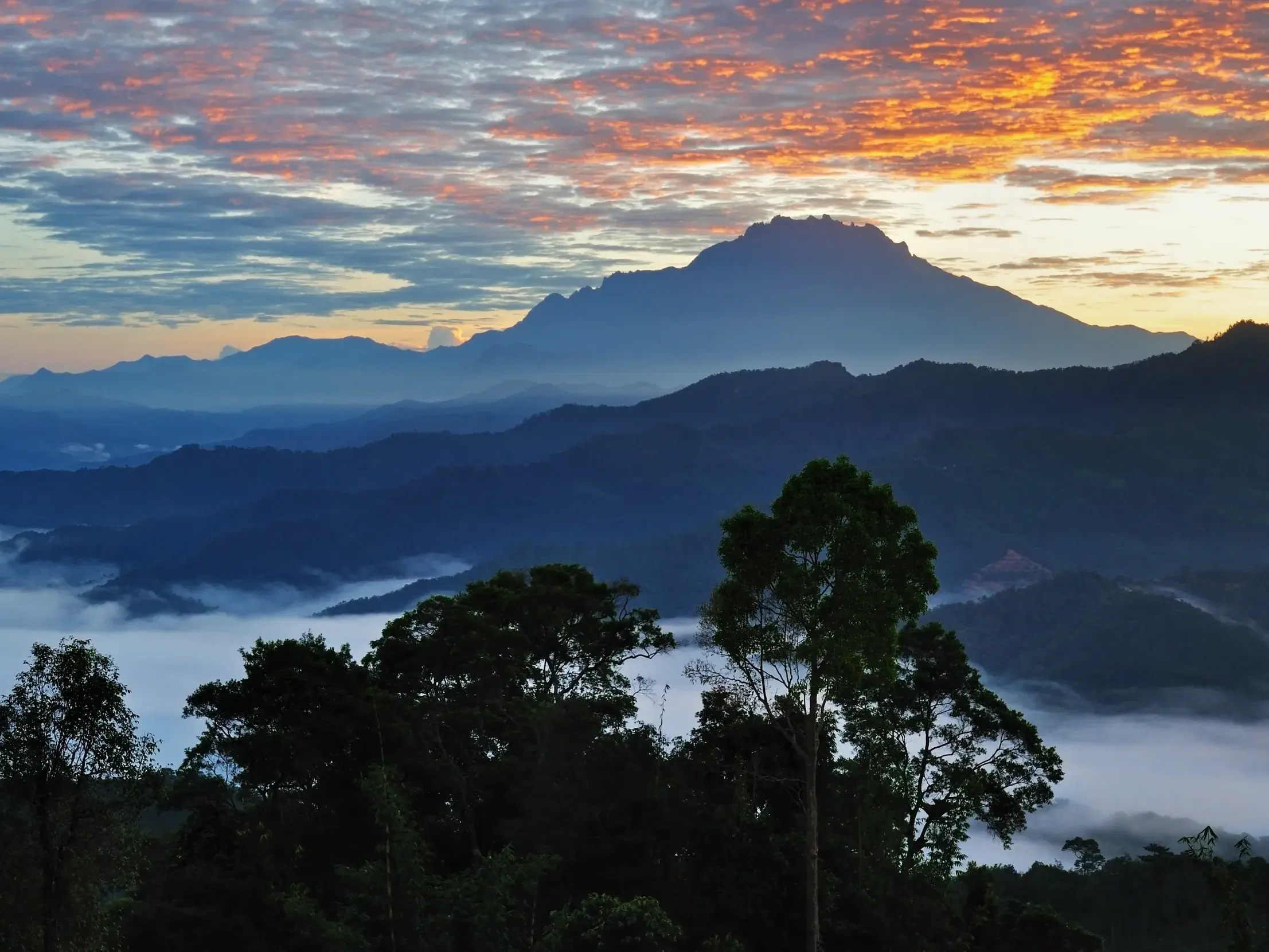 Majestätischer Sonnenaufgang über dem Mount Kinabalu auf Borneo mit Blick über nebelverhangene Täler des Regenwaldes.