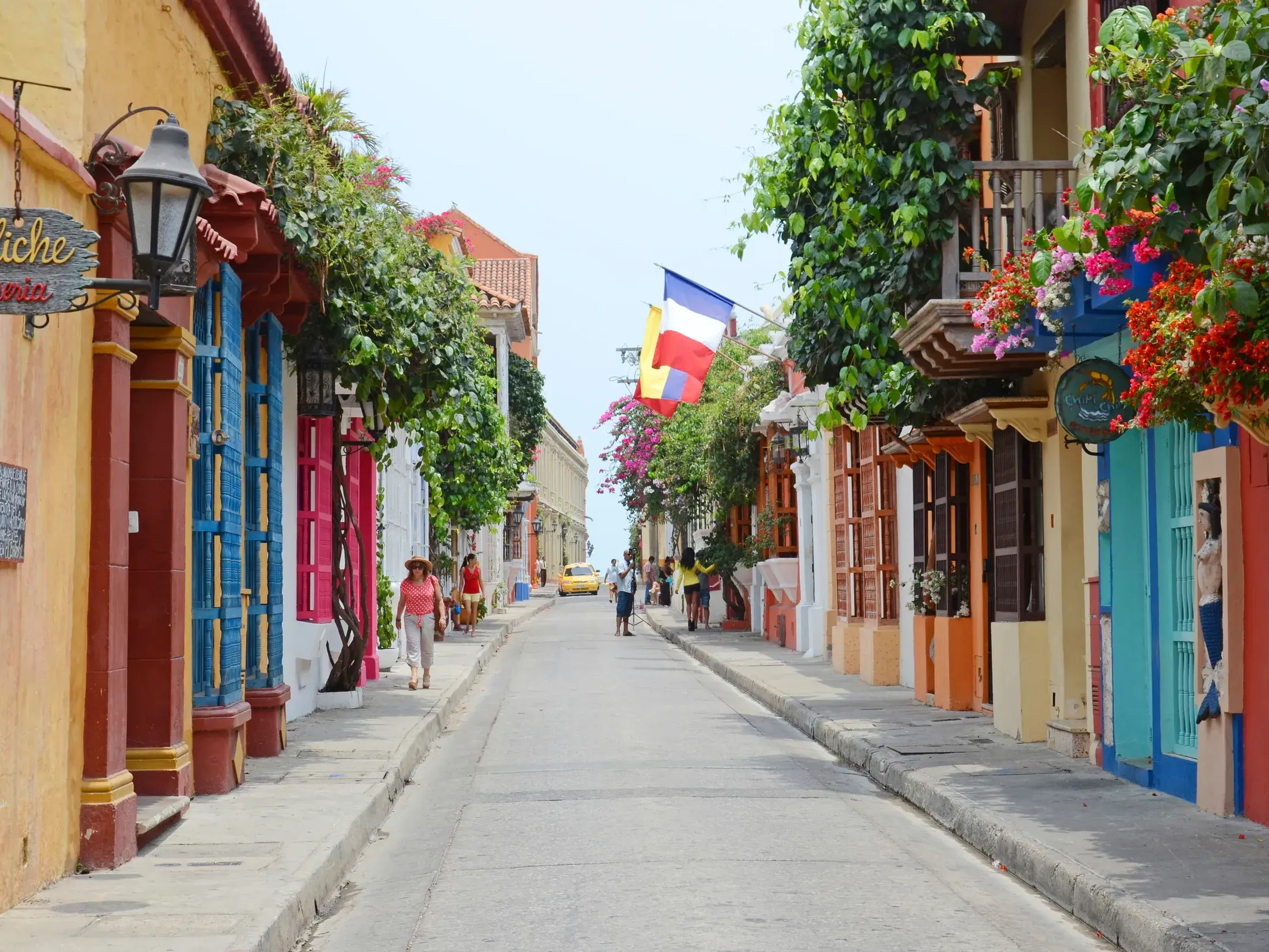 Sonnige Gasse in der Altstadt von Cartagena, gesäumt von bunten Häusern mit üppig bepflanzten Holzbalkonen.