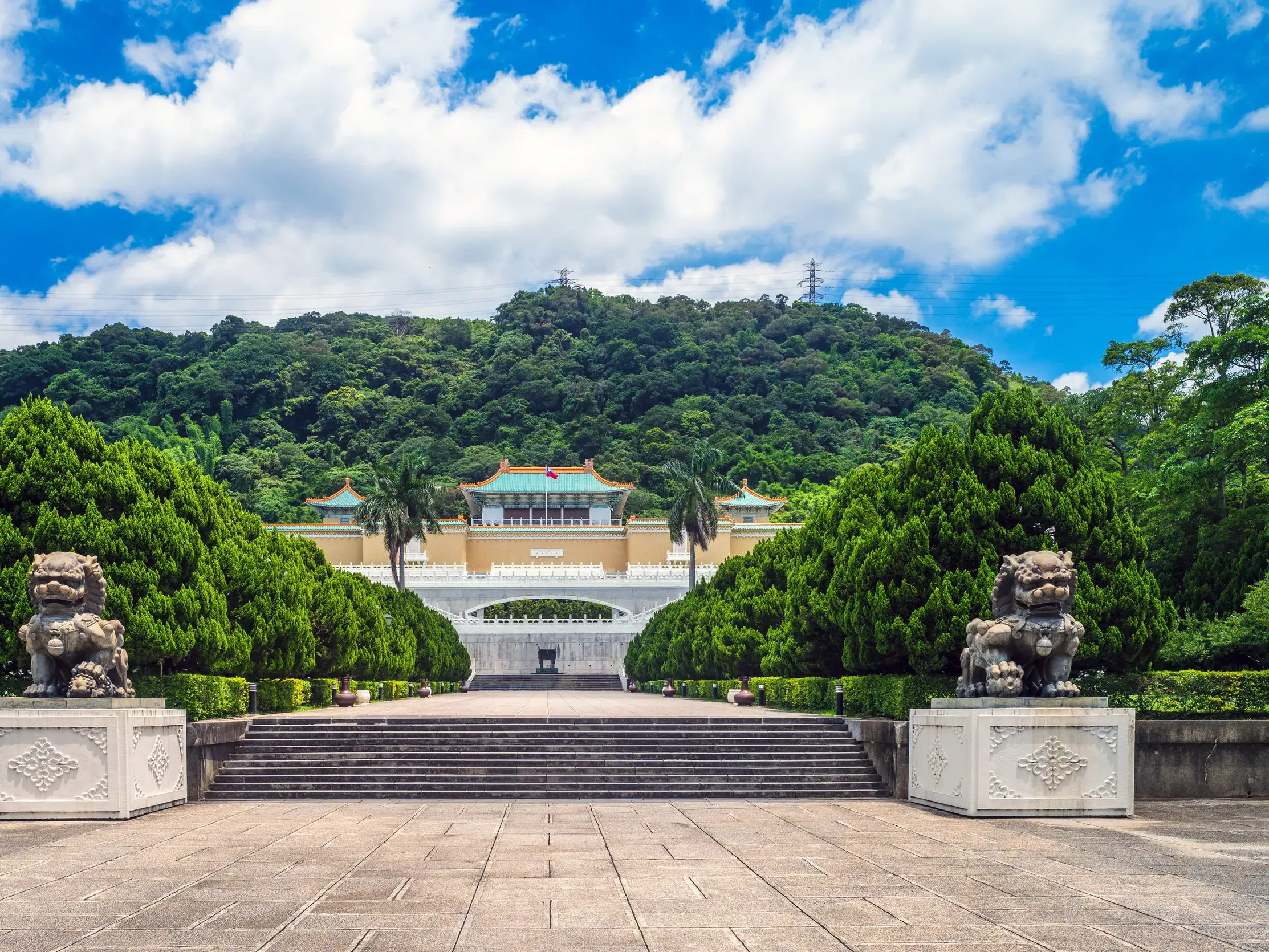 Treppenaufgang zum Palastmuseum von Taipeh mit steinernen Wächterlöwen vor grünen Bergen