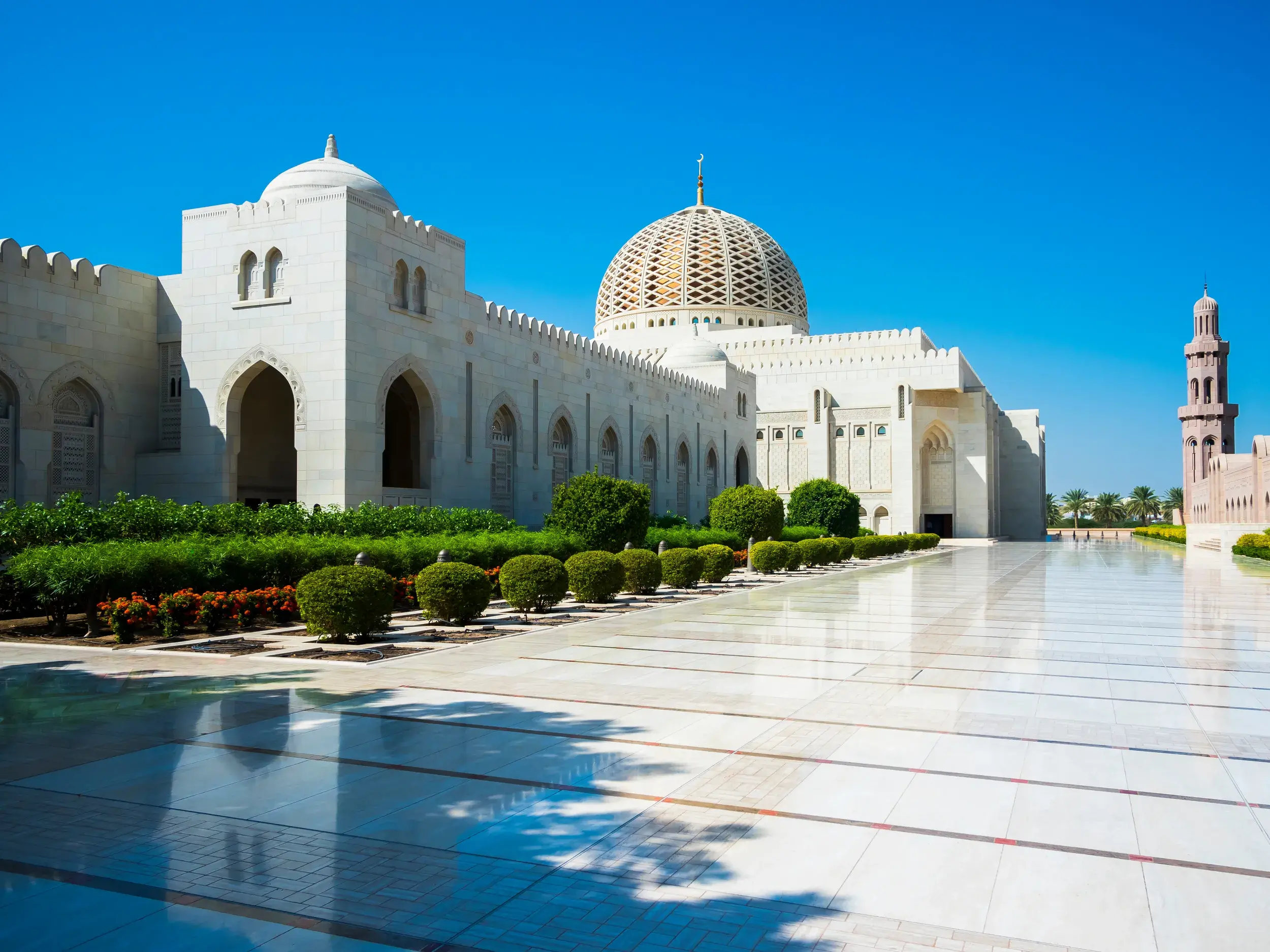 Die weiße Sultan-Qabus-Moschee in Maskat mit goldener Kuppel und poliertem Marmorhof unter strahlend blauem Himmel.