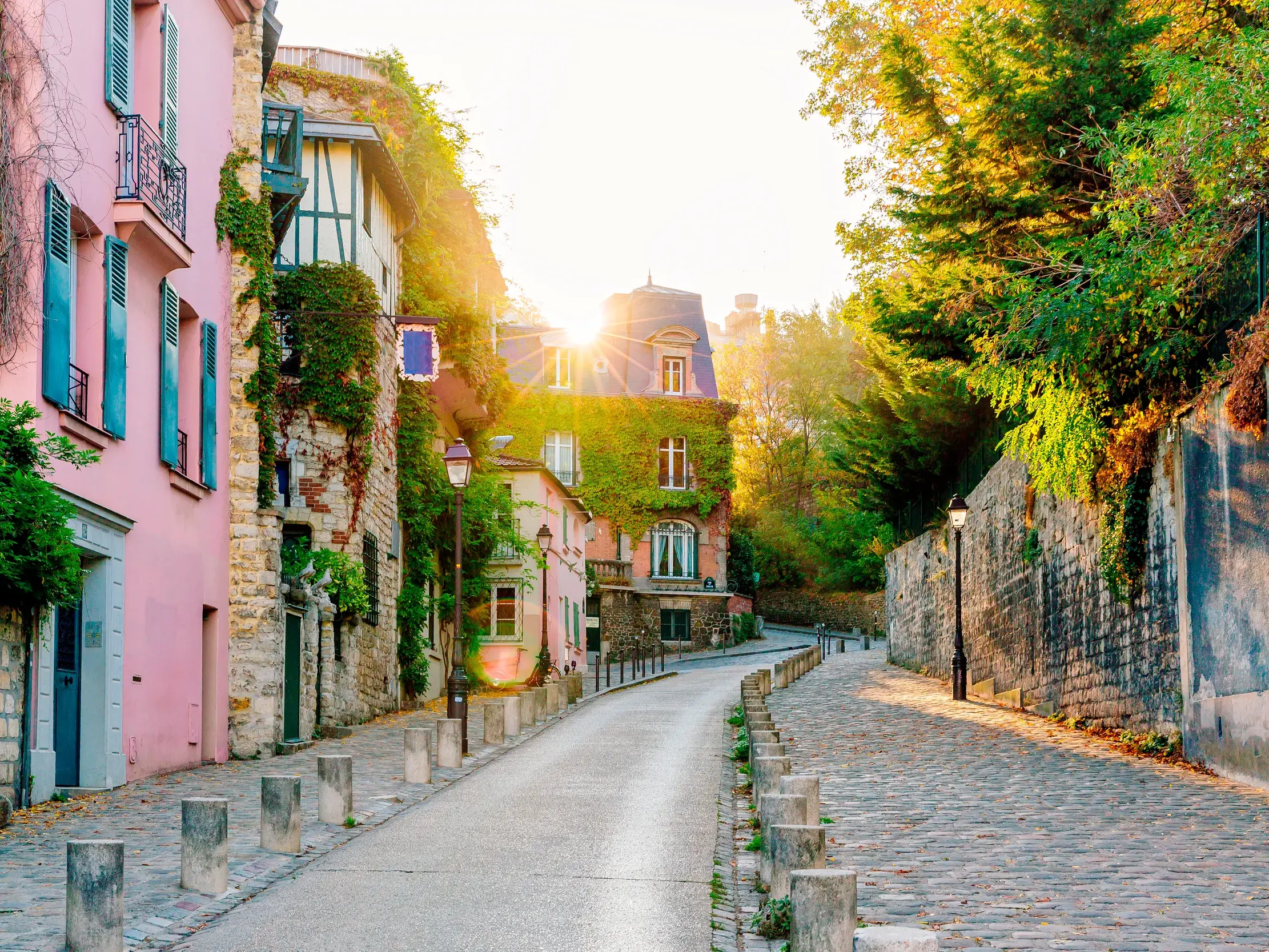 Eine idyllische Gasse auf dem Montmartre in Paris mit bunten, efeubewachsenen Häusern im goldenen Licht der Abendsonne.