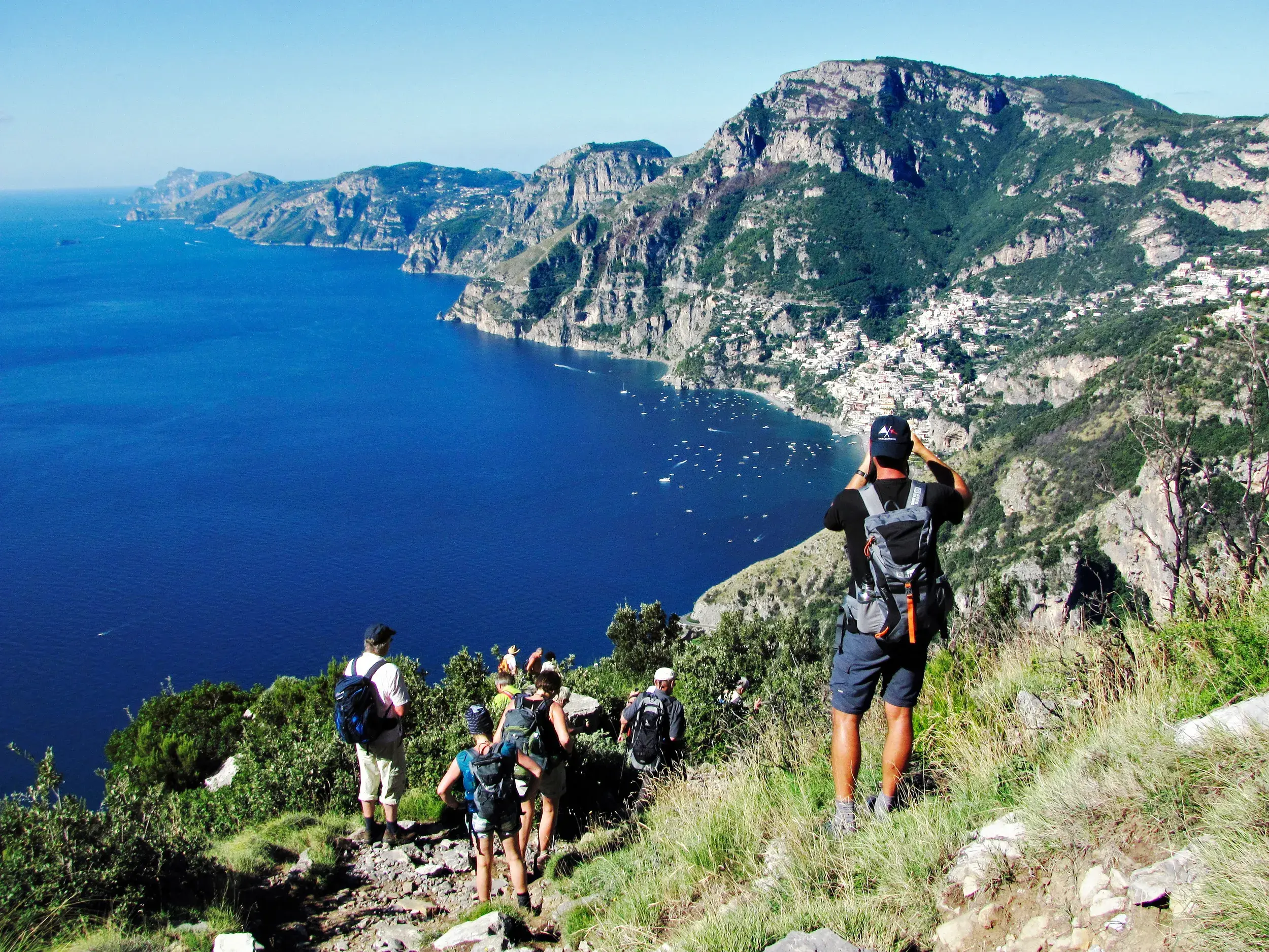 Eine Wandergruppe auf dem Sentiero degli Dei blickt auf das tiefblaue Meer und die felsige Küste bei Positano.