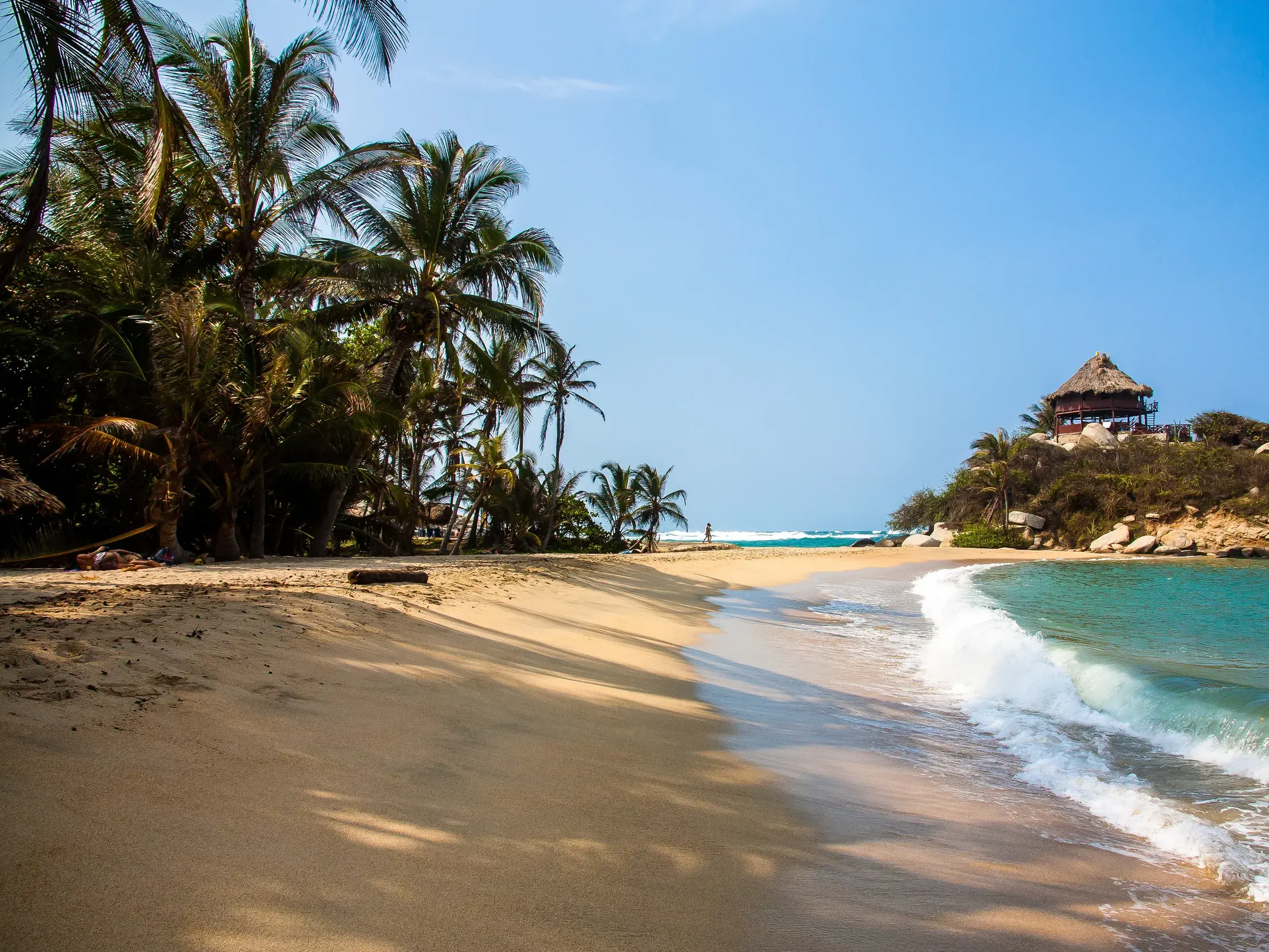 Karibischer Sandstrand Cabo de San Juan im Tayrona-Nationalpark mit Palmen und einer Hütte auf einem Felsen am Meer.