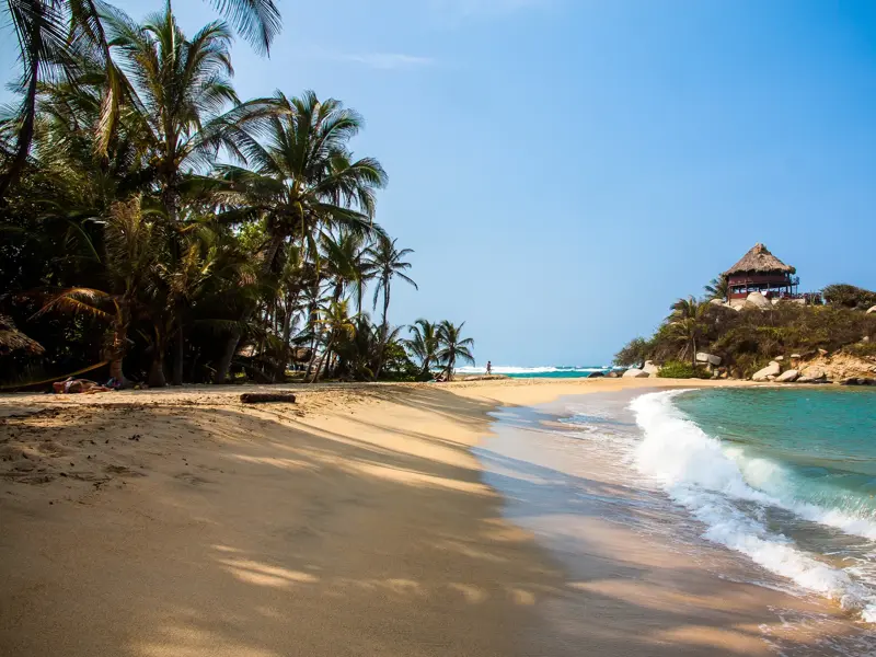 Karibischer Sandstrand Cabo de San Juan im Tayrona-Nationalpark mit Palmen und einer Hütte auf einem Felsen am Meer.