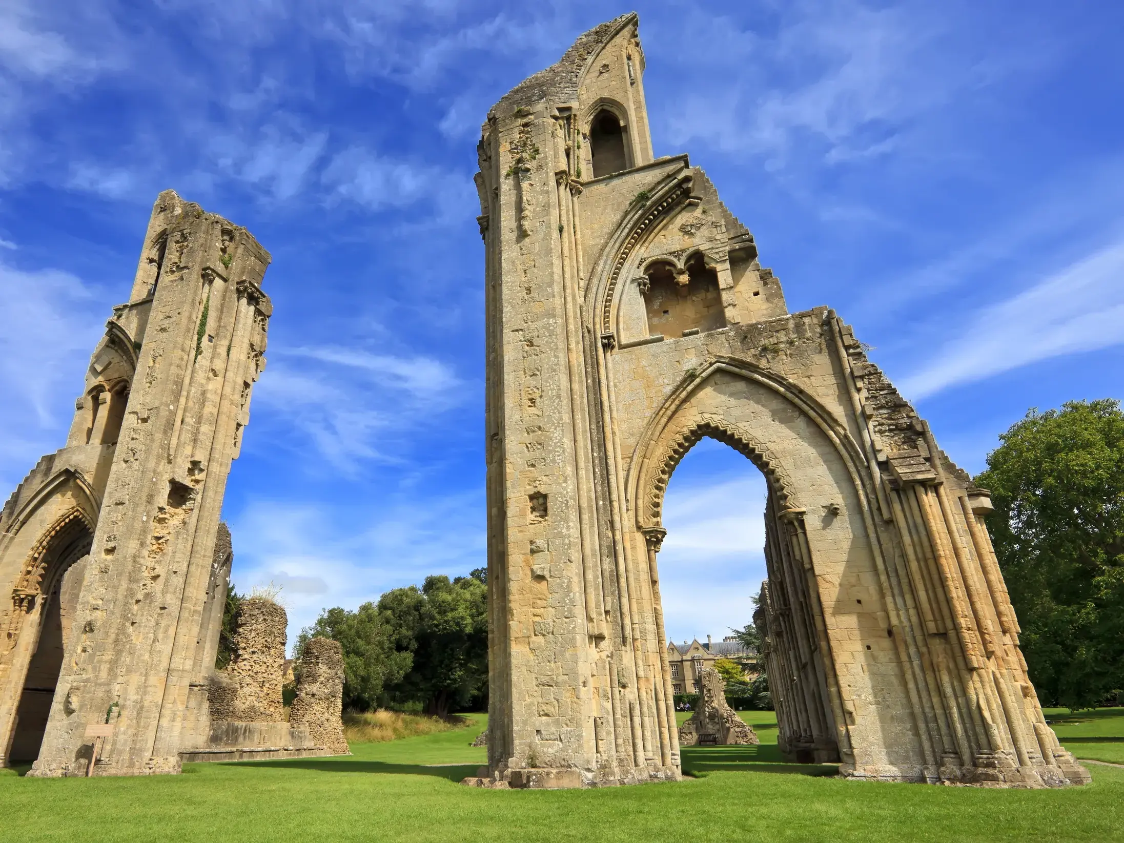 Die majestätischen, gotischen Ruinen der Glastonbury Abbey ragen auf einer grünen Wiese in den blauen Himmel Südenglands.