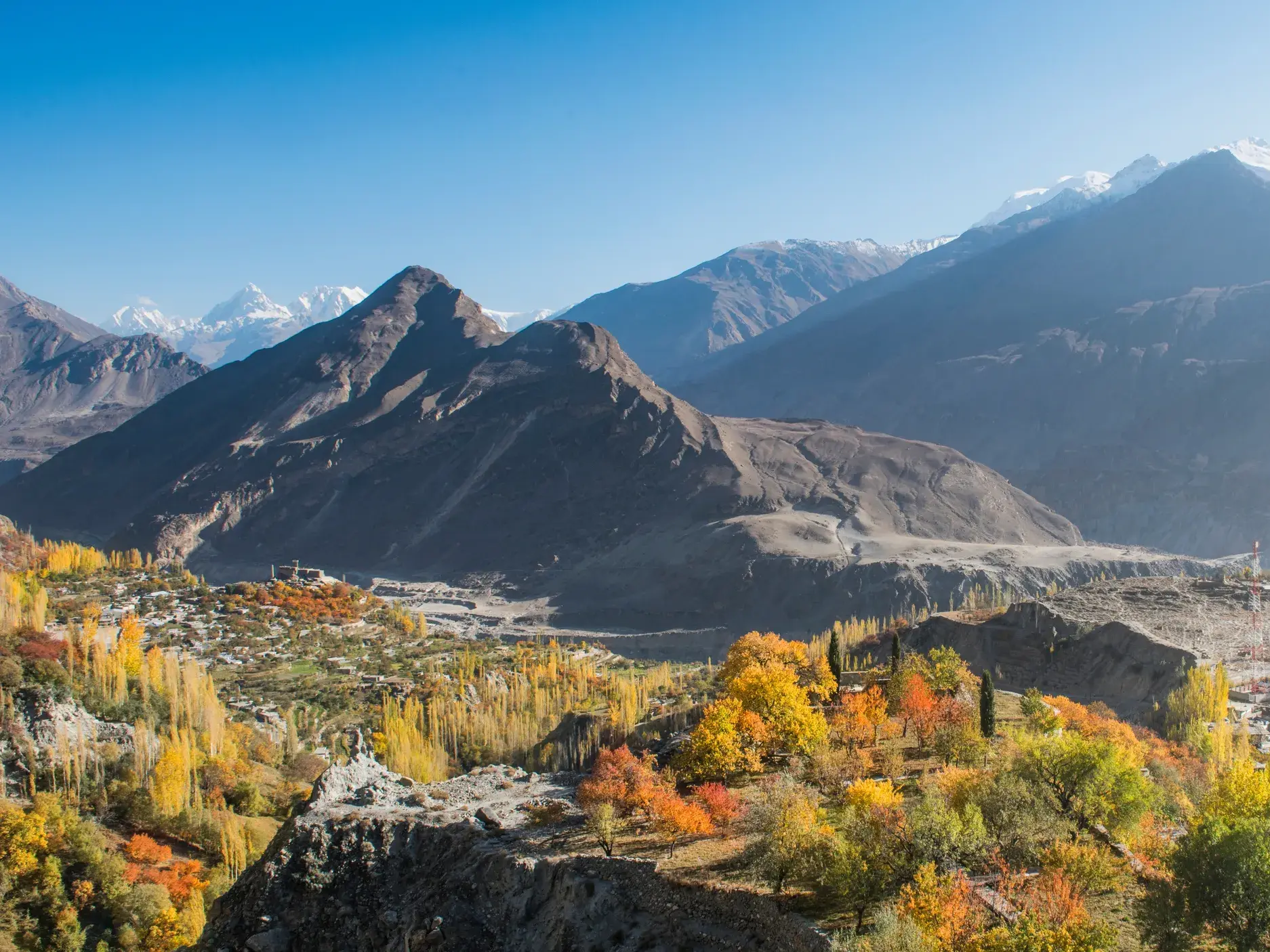 Panoramablick auf das Hunzatal in Pakistan mit farbenfrohen Herbstbäumen und den schneebedeckten Gipfeln des Karakorum.