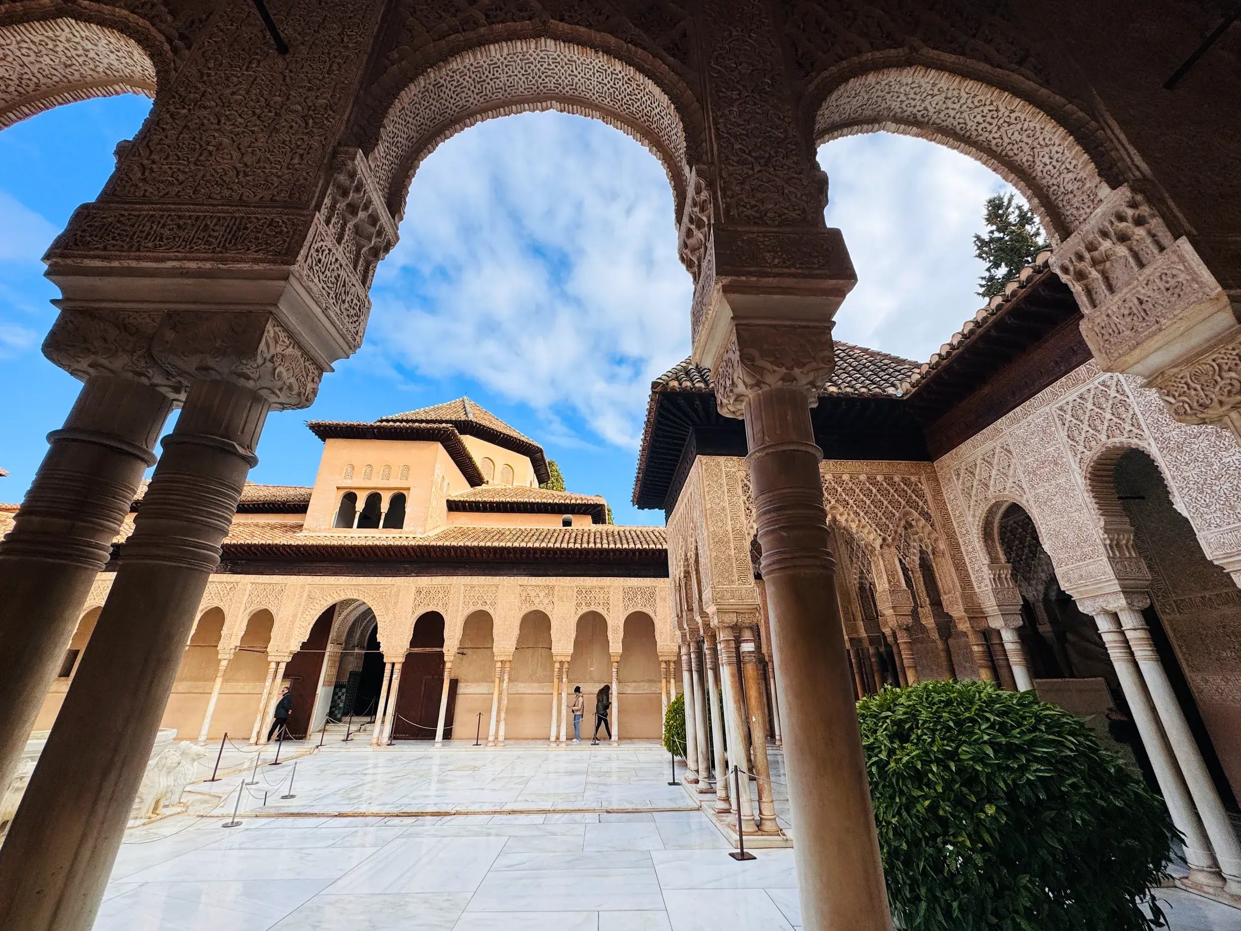 Blick durch Bögen mit filigranen Arabesken in einen sonnigen Innenhof der Alhambra, der Maurenburg von Granada.