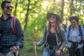 Eine junge Frau lacht bei einer Gruppenreise in Ecuador, während sie mit Wanderstock und Rucksack durch einen Wald wandert.