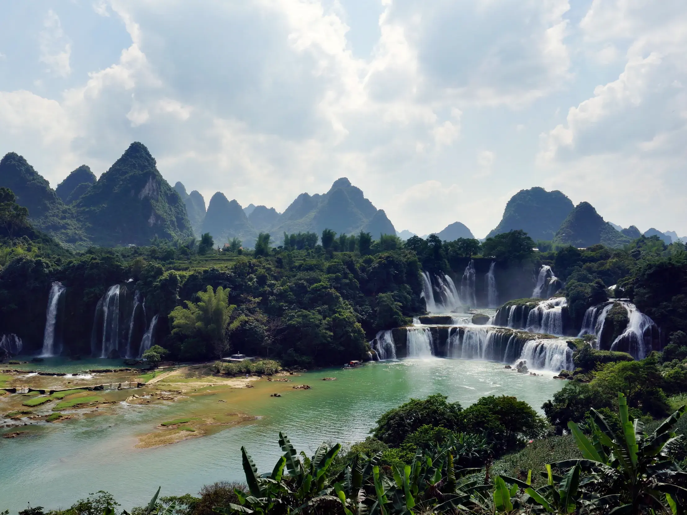 Tosende Bản-Gioc-Wasserfälle stürzen in Kaskaden in einen türkisen Fluss, umgeben von tropischer Vegetation und Karstbergen.
