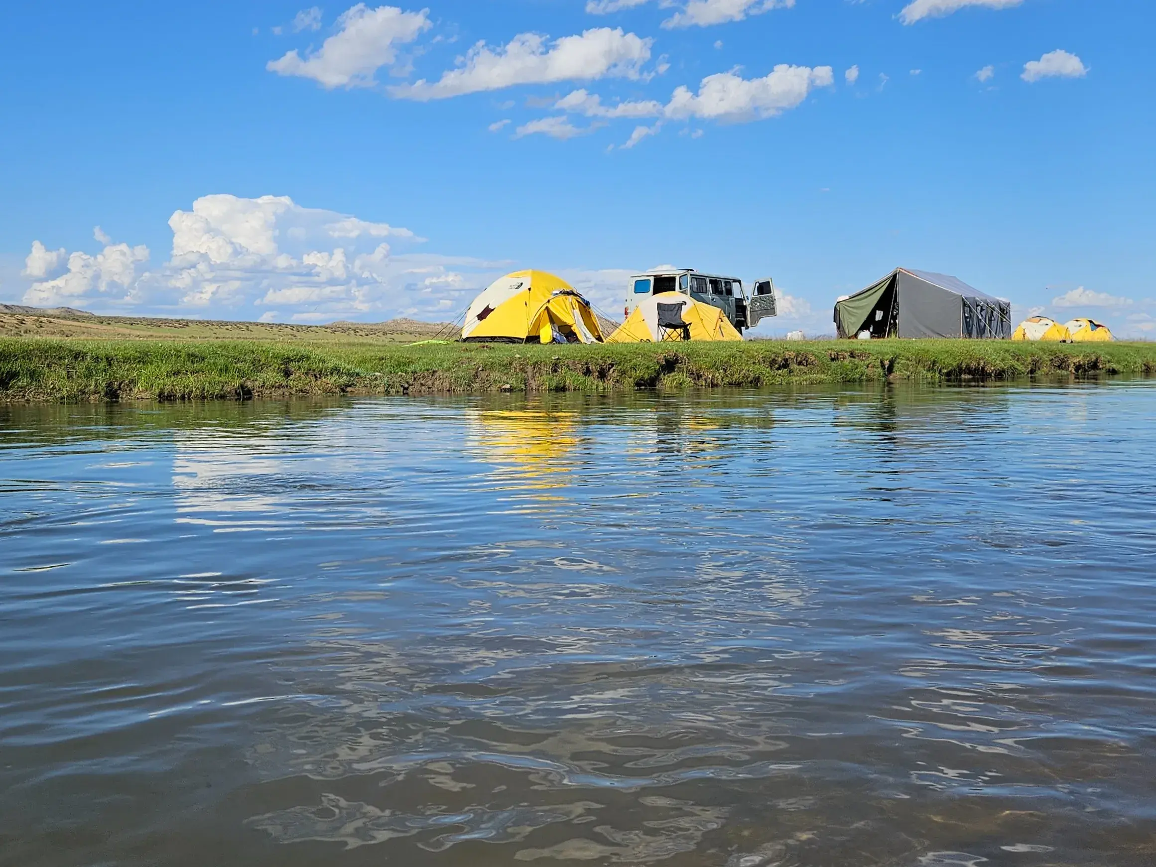 Zelte und ein Fahrzeug eines Trekking-Camps am Ufer des Flusses Zavkhan in der weiten Steppe der Mongolei.