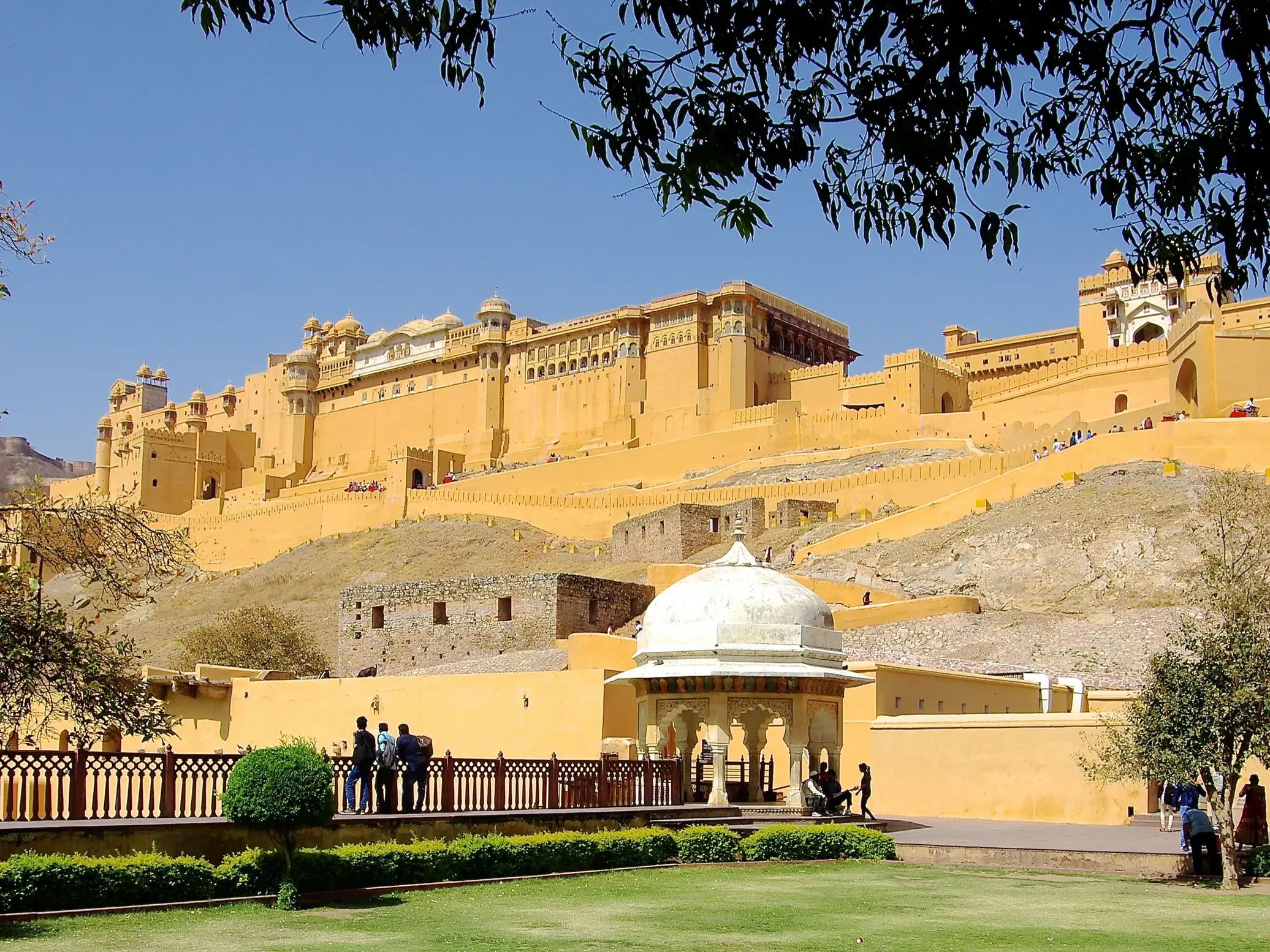 Eine Marco Polo Reisegruppe blickt vom Garten aus auf das imposante, gelbe Fort Amber, das sich in Jaipur einen Hügel hinaufzieht.