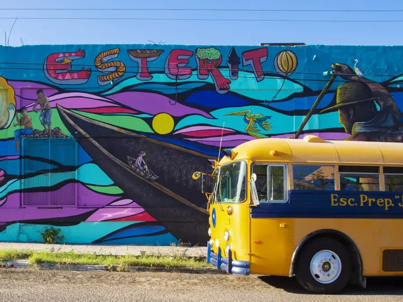 Gelber amerikanischer Schulbus parkt vor farbenfroher Straßenkunst mit Meeresmotiven im Stadtviertel El Esterito in La Paz.