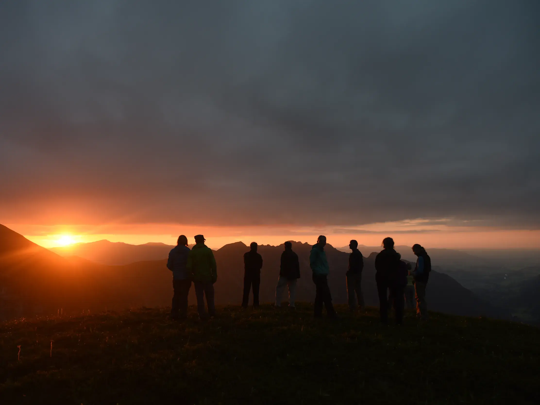 Eine Wandergruppe auf der Alpenüberquerung E5 beobachtet den farbenprächtigen Sonnenuntergang über dem Arlberg-Panorama.