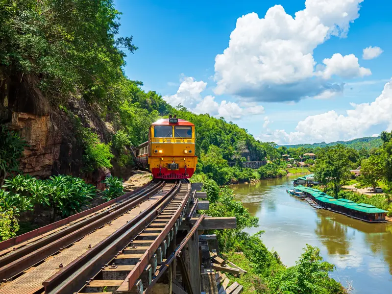 Die historische Todeseisenbahn fährt auf einem Viadukt durch die Dschungellandschaft entlang des River Kwai in Thailand.
